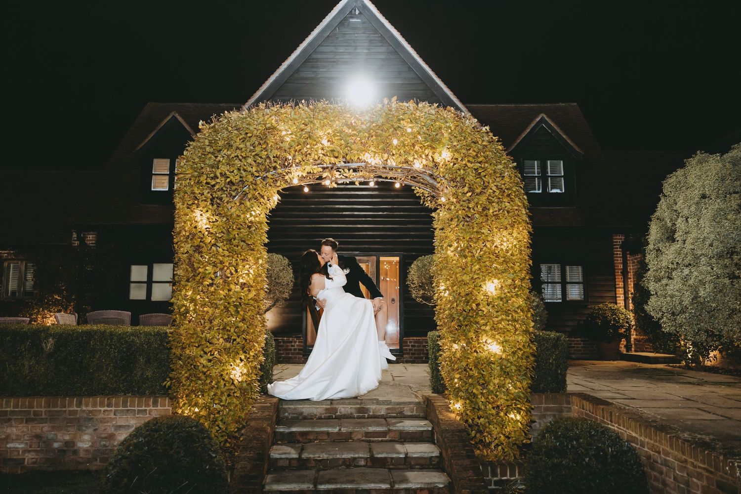 Wedding ceremony setup at night with golden lit archway and glowing decorative elements.