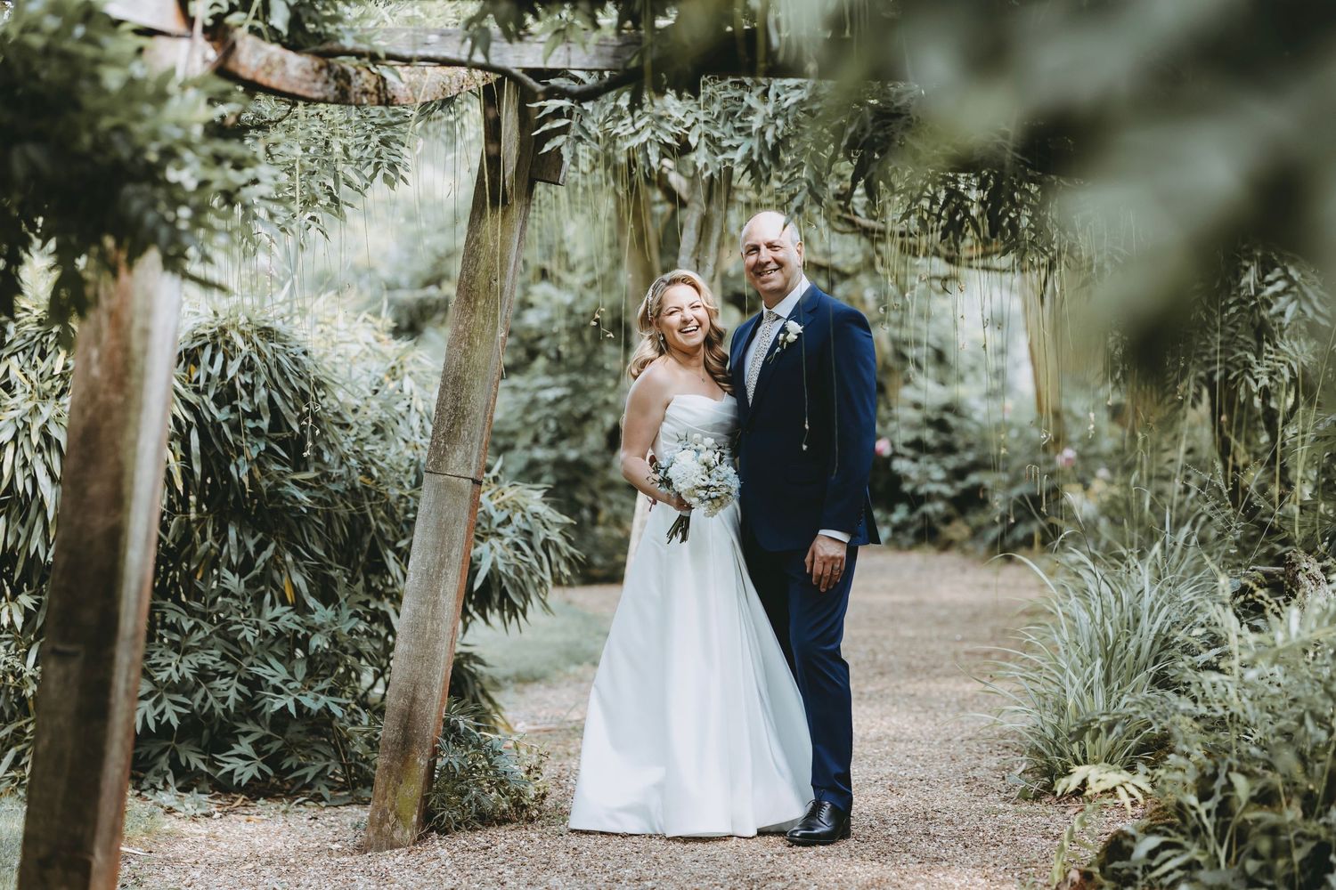 Couple poses for wedding portraits in lush garden setting.