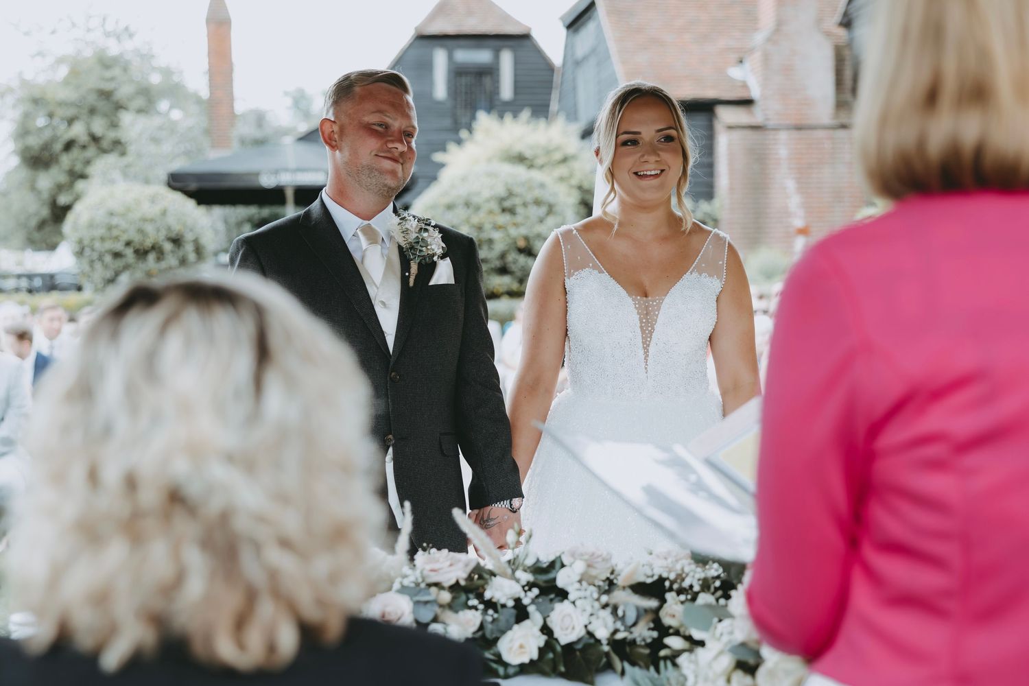 Couple exchanges vows at outdoor ceremony with white floral arrangements.