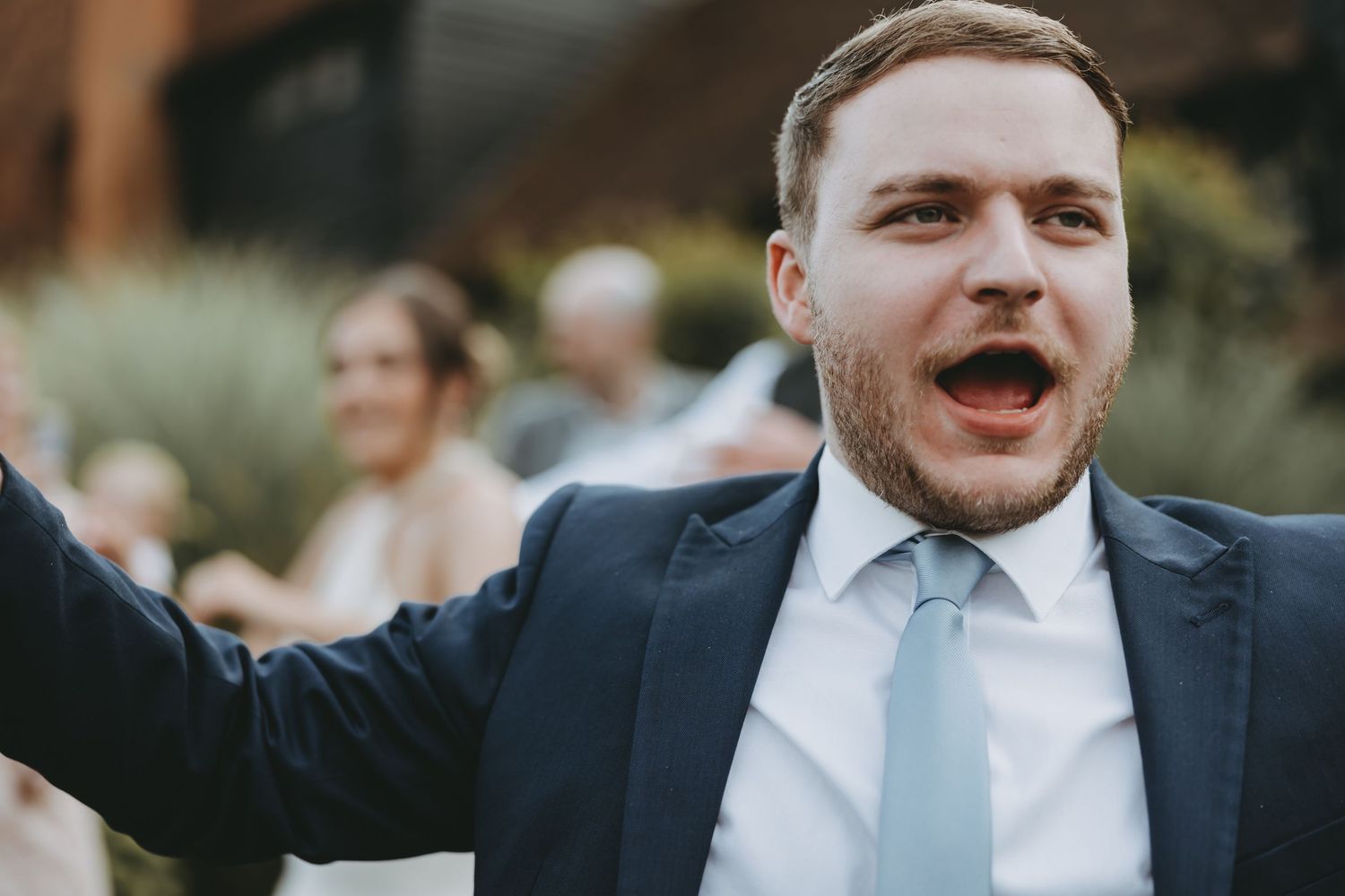 Wedding guests in formal attire celebrate with enthusiasm at an outdoor venue.