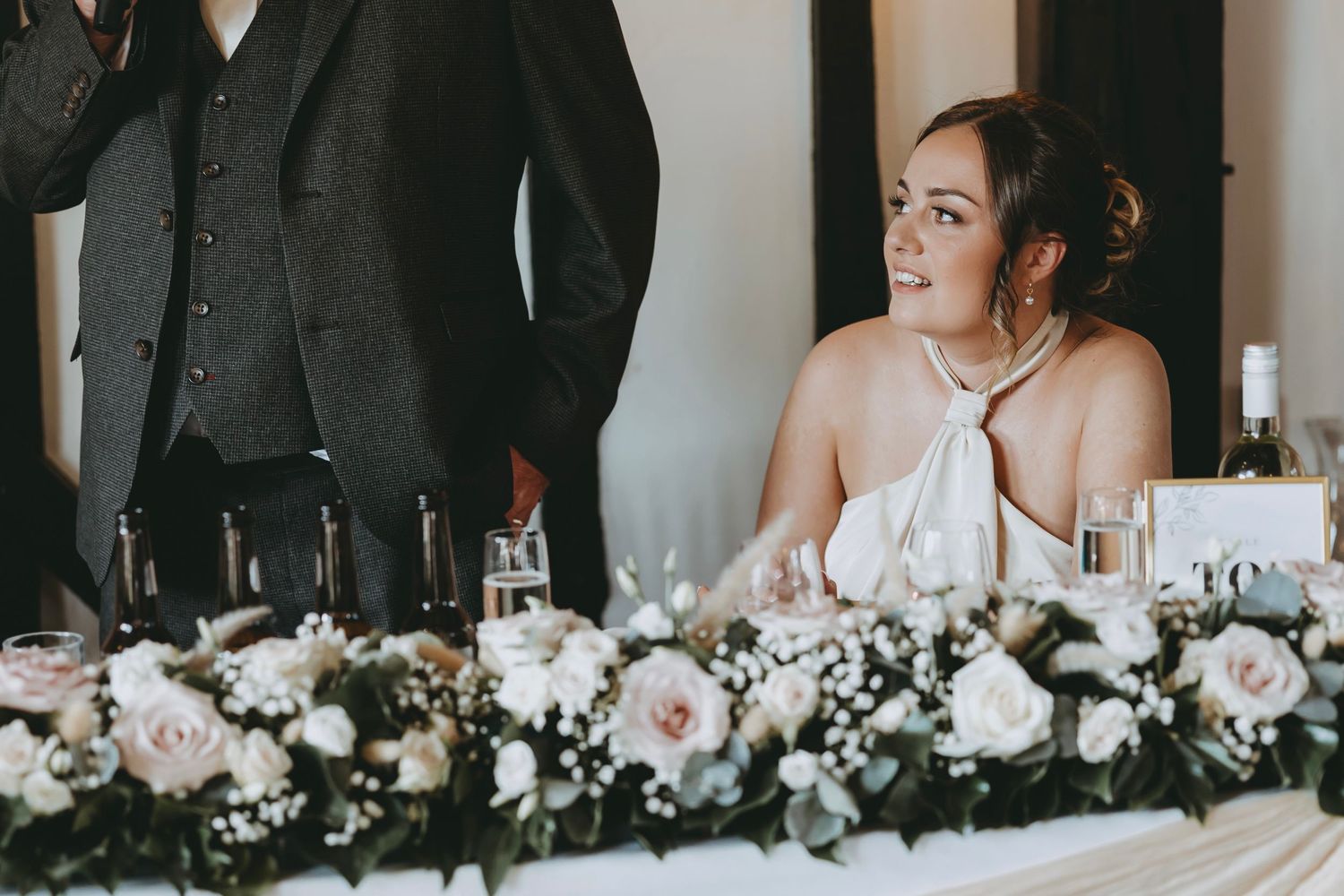 Wedding party seated at long banquet table with white rose floral arrangements and black and white decor.