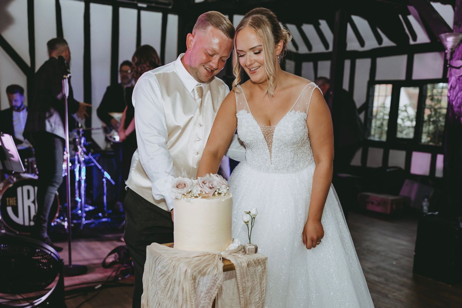 Wedding couple cutting their elegant white cake during reception in rustic barn venue.