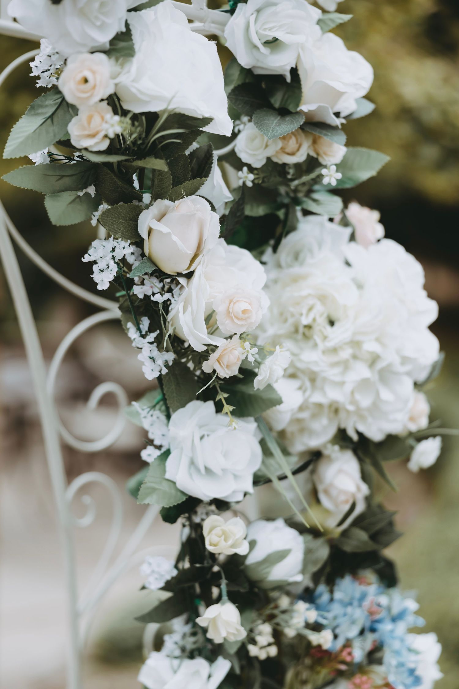 Elegant white floral wedding arch decoration with roses and hydrangeas against a natural backdrop.