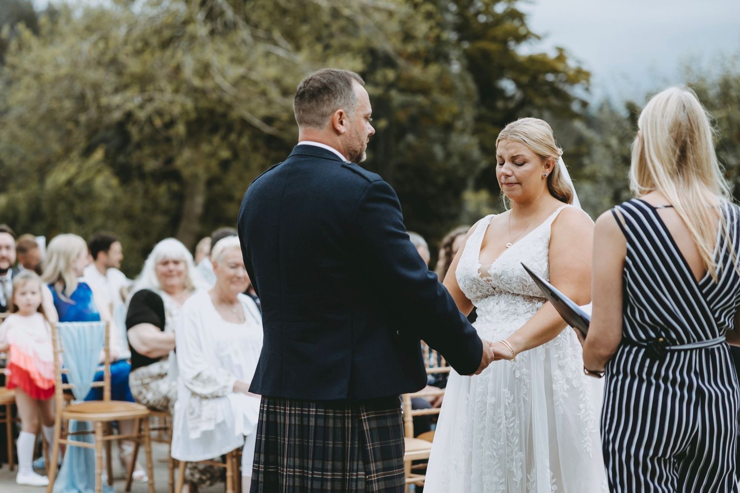 Guests mingle at an outdoor wedding venue with stone walls and greenery in the background.