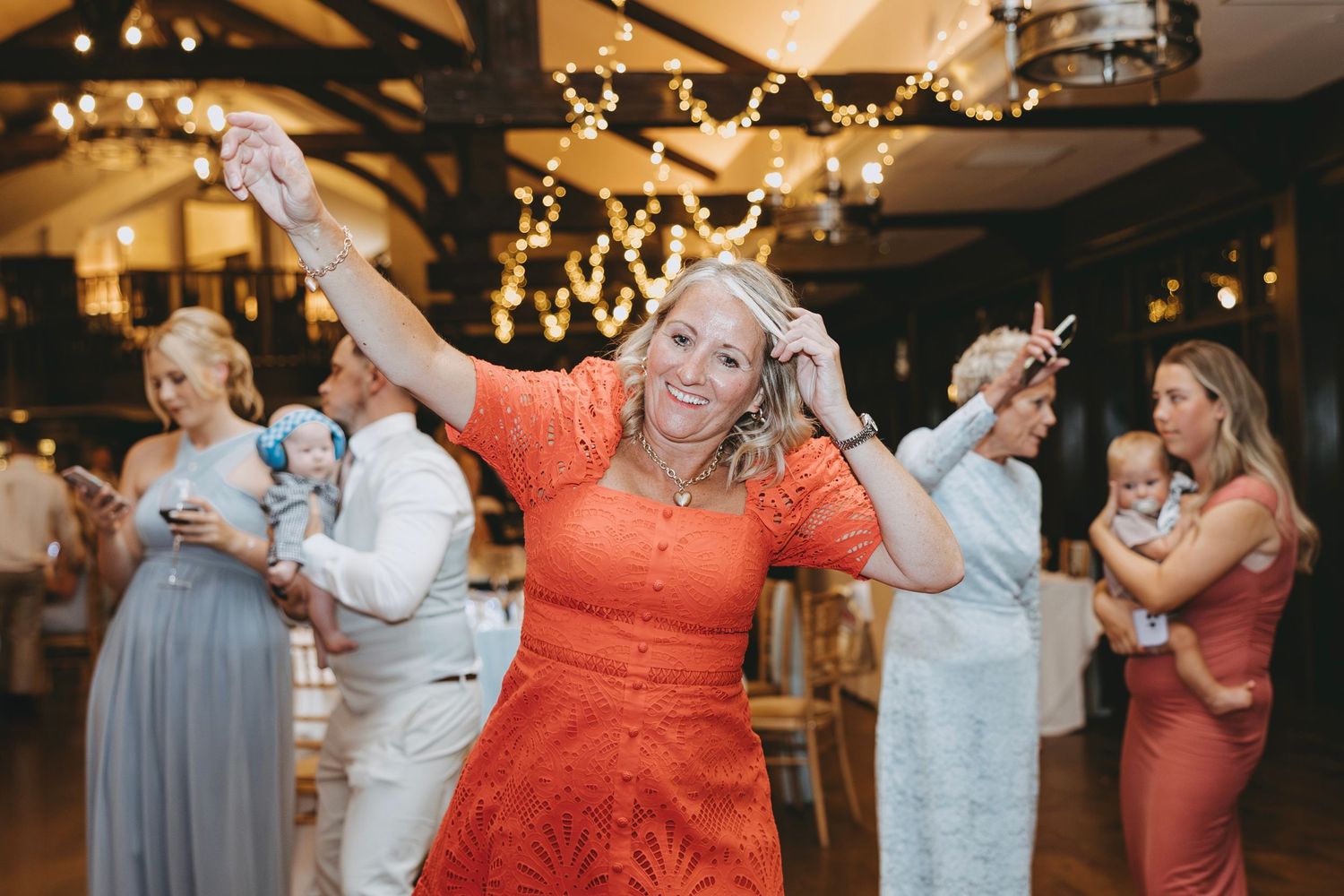 Wedding guests dancing in formal attire under warm lighting at an indoor reception venue.