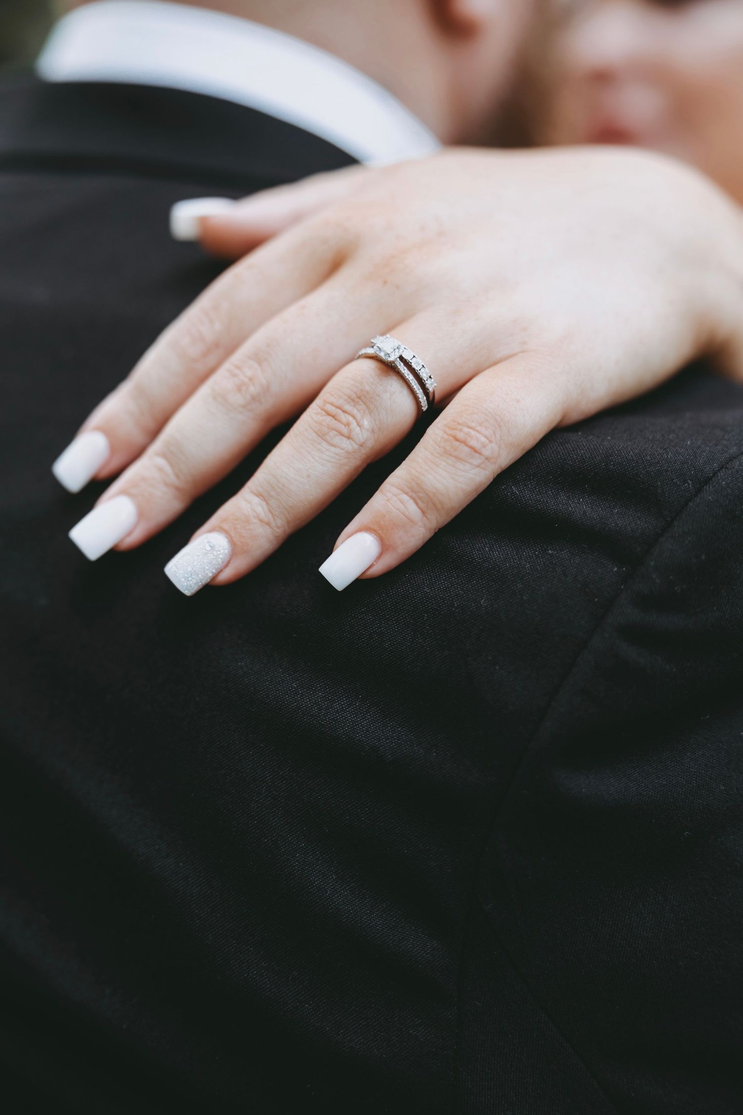Close-up of a bride's manicured hand with wedding ring resting on black fabric.