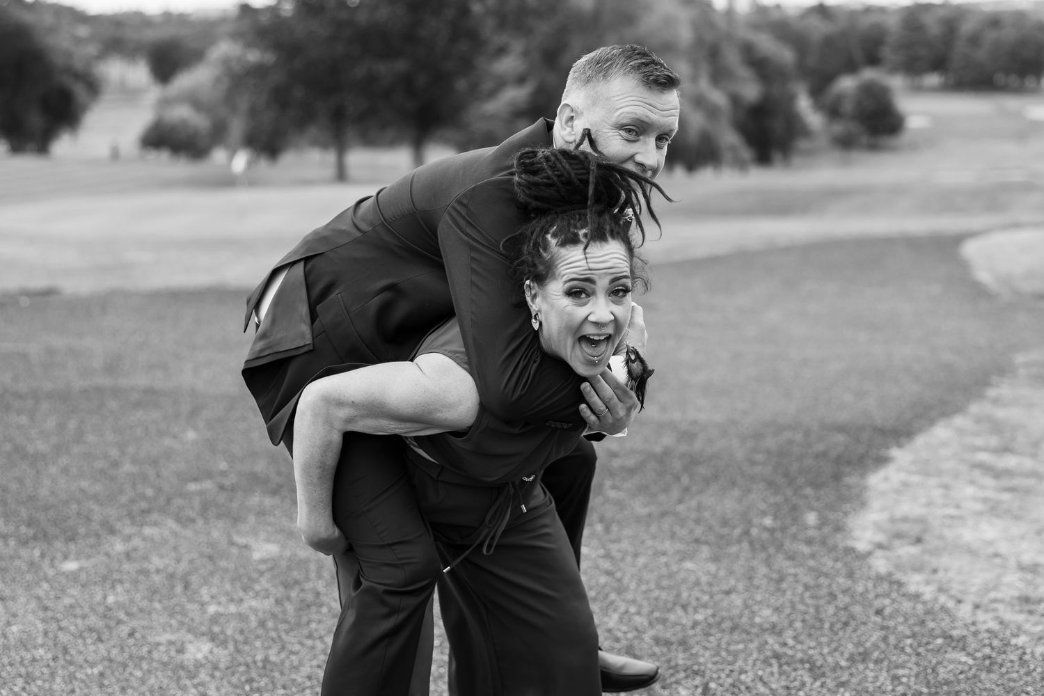 Playful black and white photo of a piggyback ride during wedding celebrations.