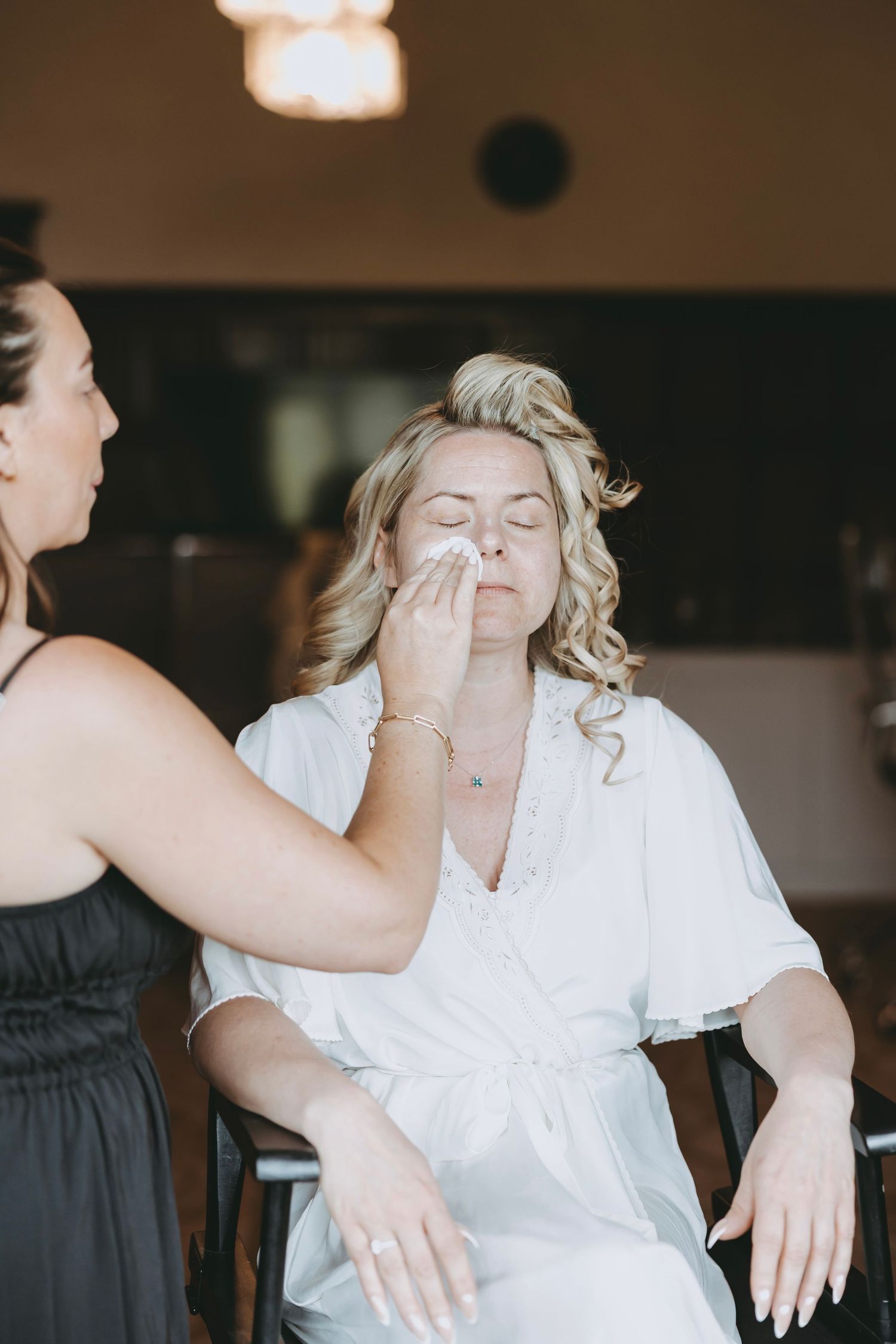 A person in a white robe getting their makeup done while sitting in a chair.