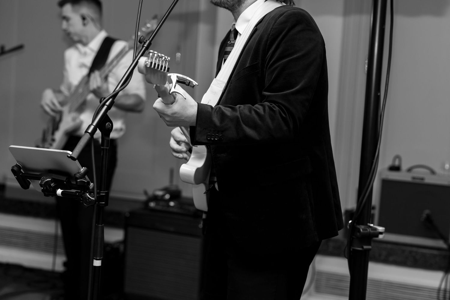 Black and white photo of a guitarist performing on stage with microphone stands and equipment visible.