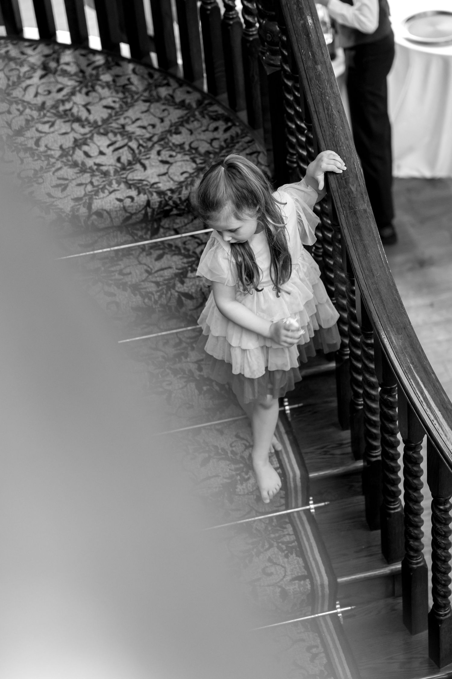 Young girl in white dress sitting on ornate staircase at wedding venue.