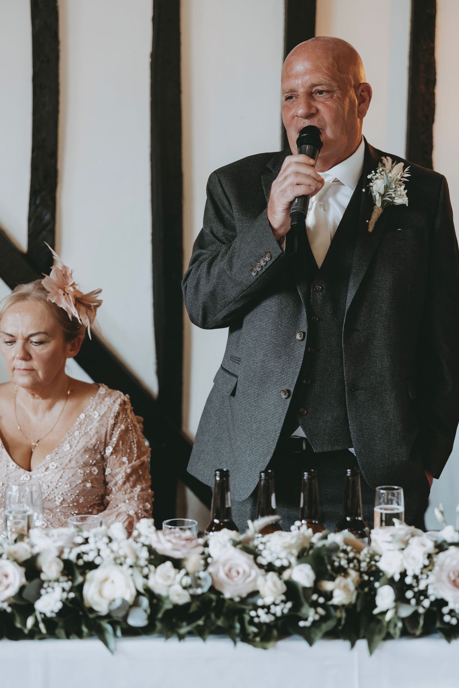 Wedding reception guests seated at head table with elegant white floral centerpiece decorations.