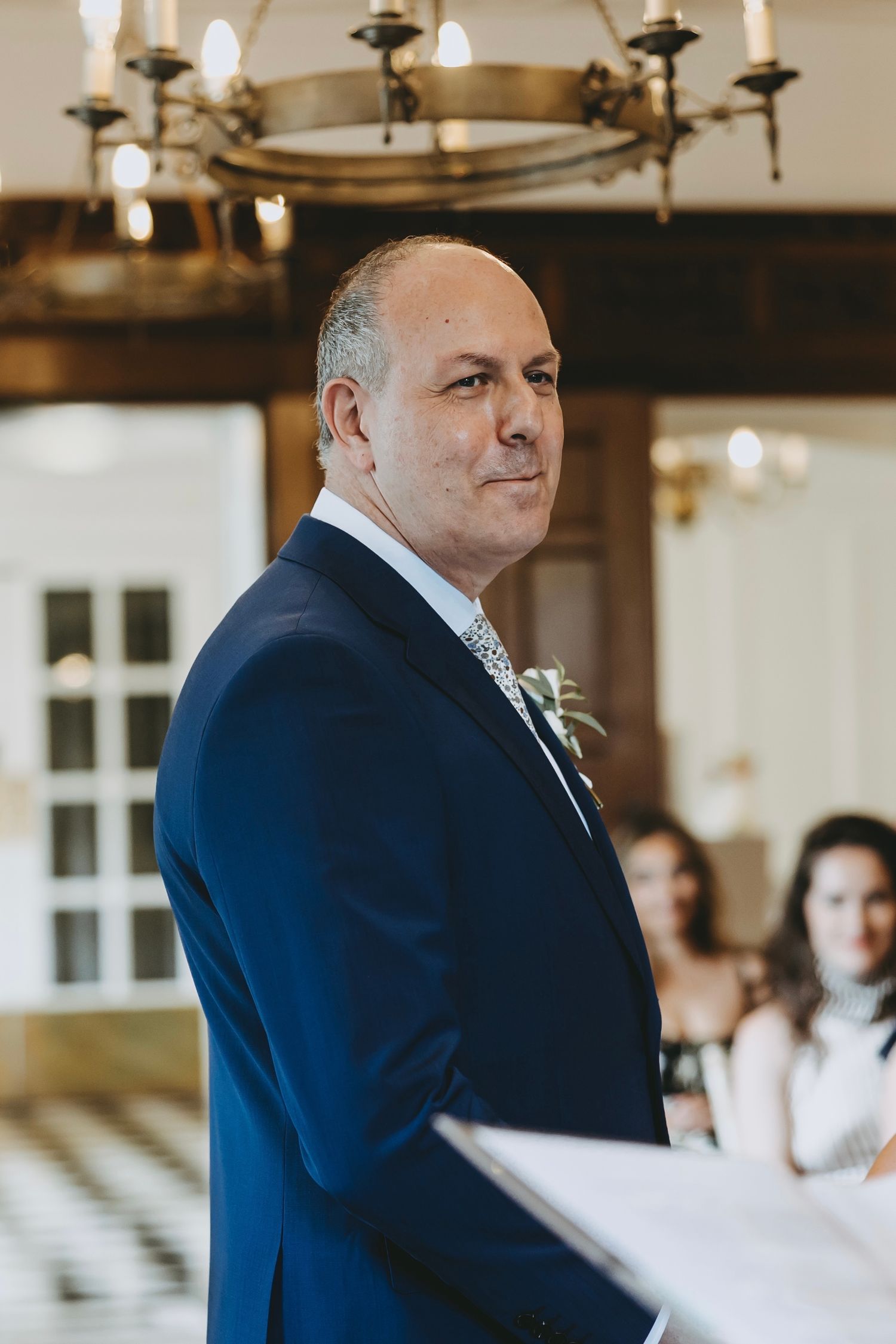 Side profile view of groom in navy suit during wedding ceremony in elegant indoor setting.