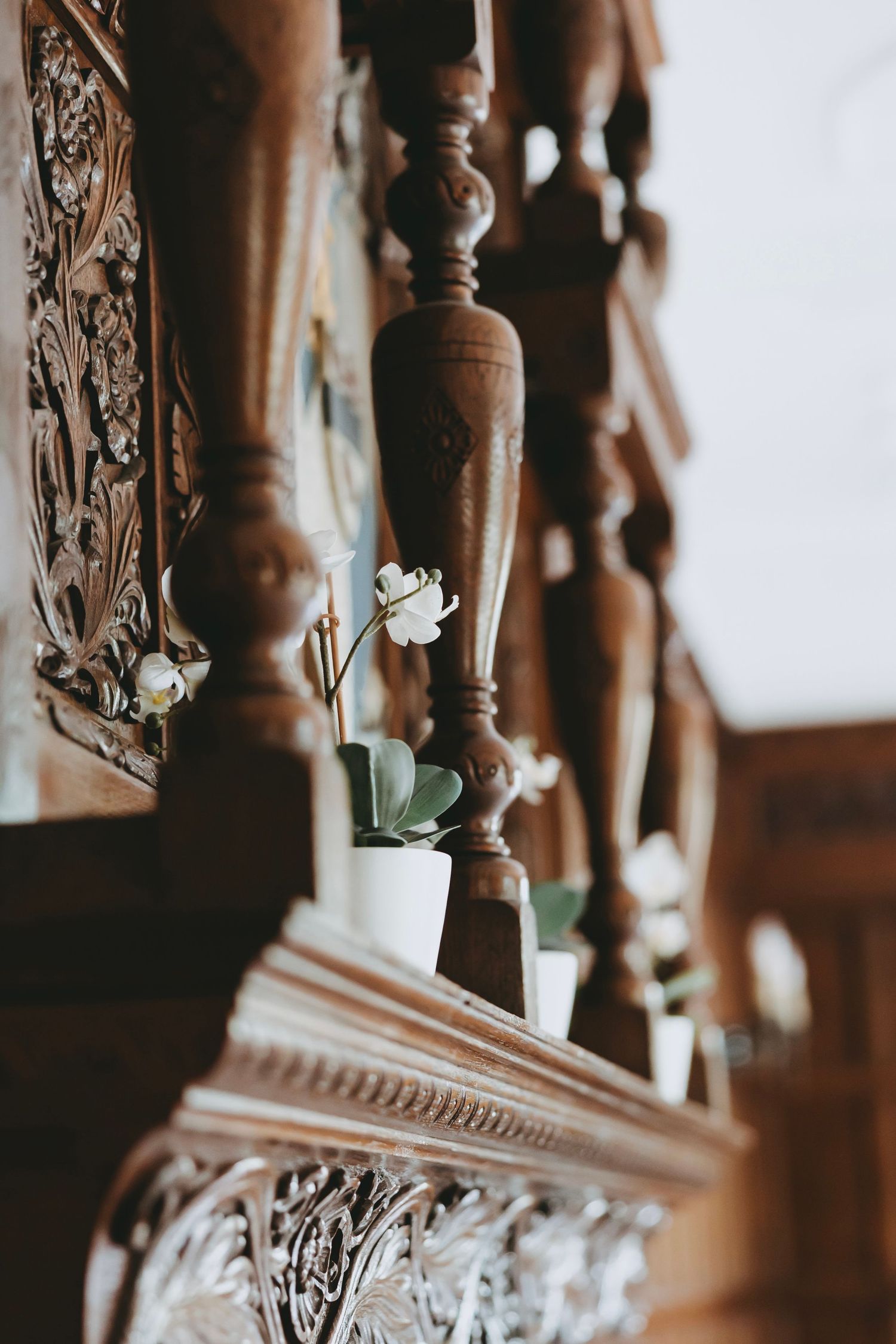 Close-up view of ornate wooden staircase balusters and railing details with carved decorative elements in sepia tones.