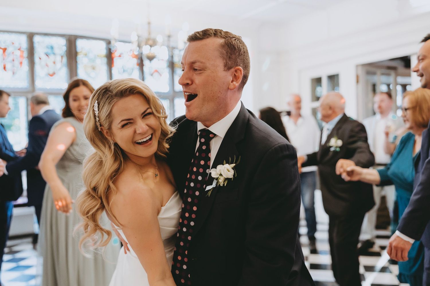Celebratory dancing and laughter at an elegant indoor wedding reception at Fanhams Hall, Ware, Hertfordshire.