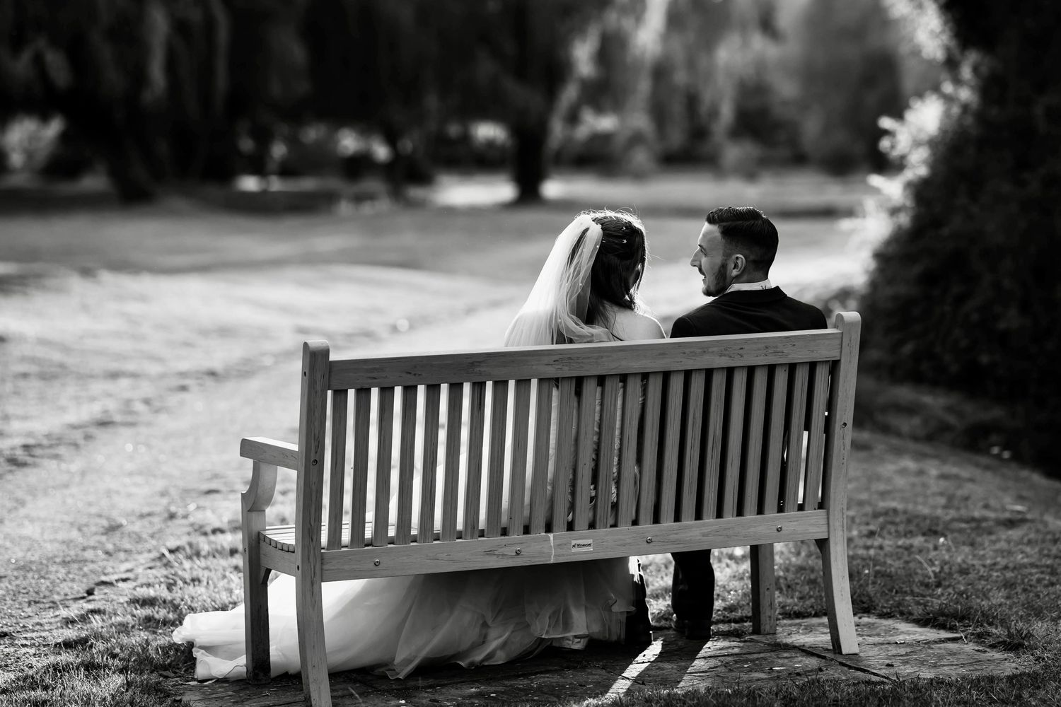 A couple sits together on a wooden park bench in a romantic black and white photograph.