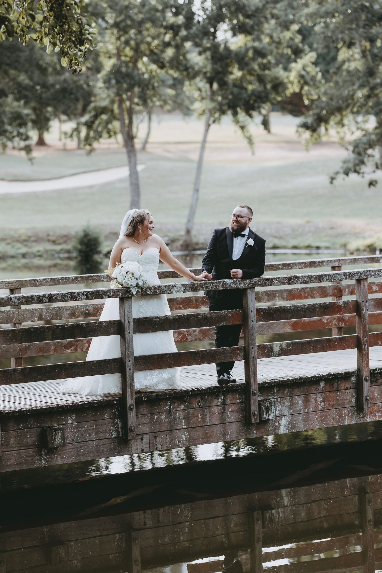 A romantic moment captured on a rustic wooden bridge over water with trees in the background at Essendon Golf Club, Hertfordshire.