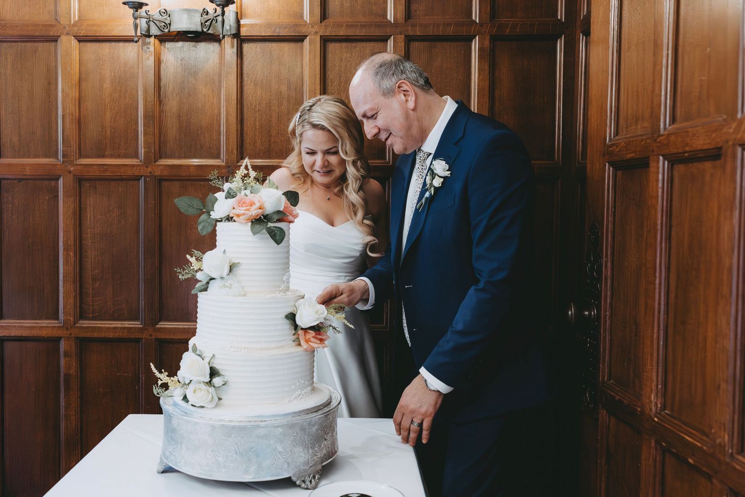 Newlyweds share an intimate moment while cutting their white floral-decorated wedding cake.