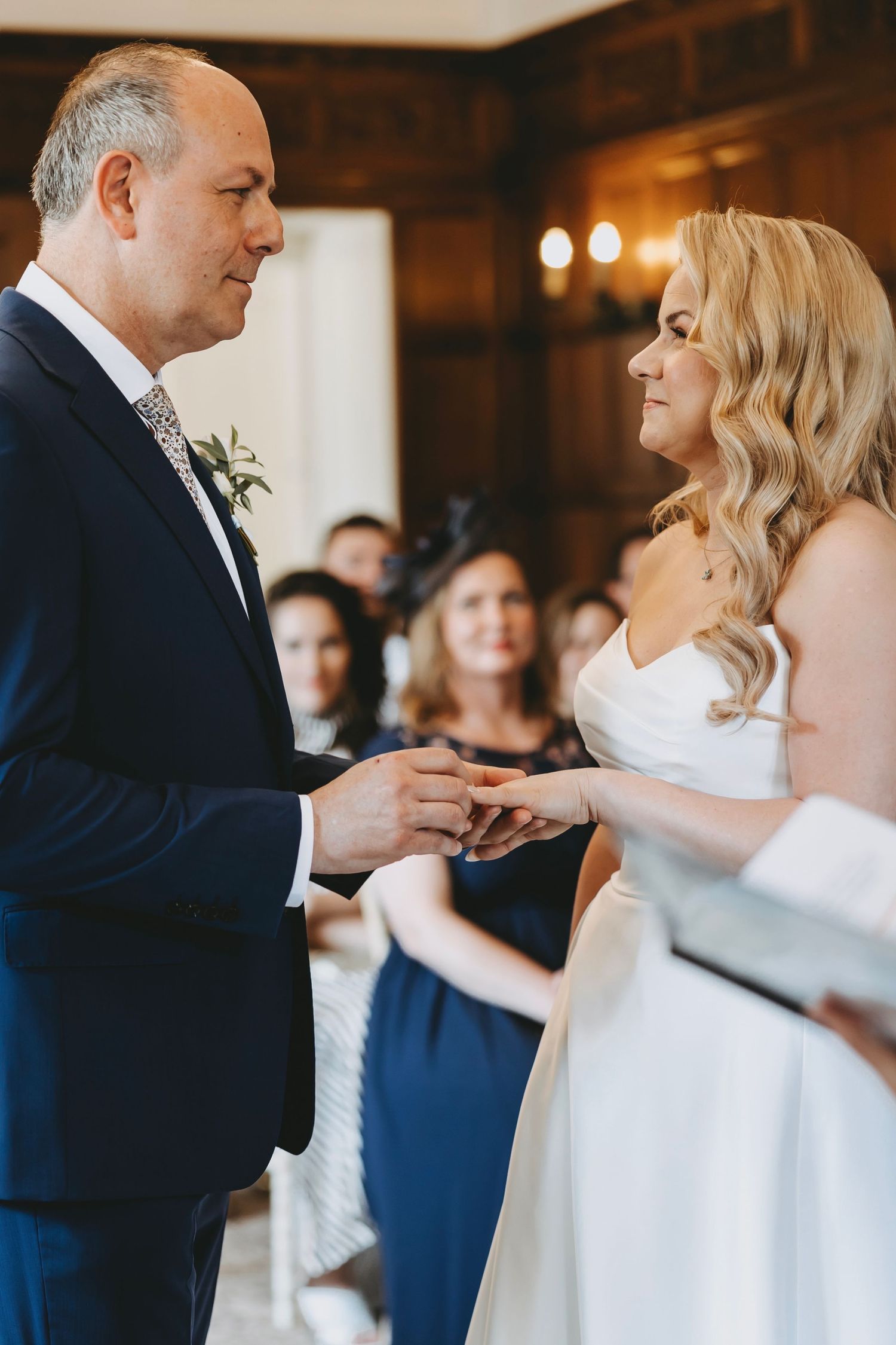 An intimate wedding ceremony moment captured in a wood-paneled room with chandelier lighting.