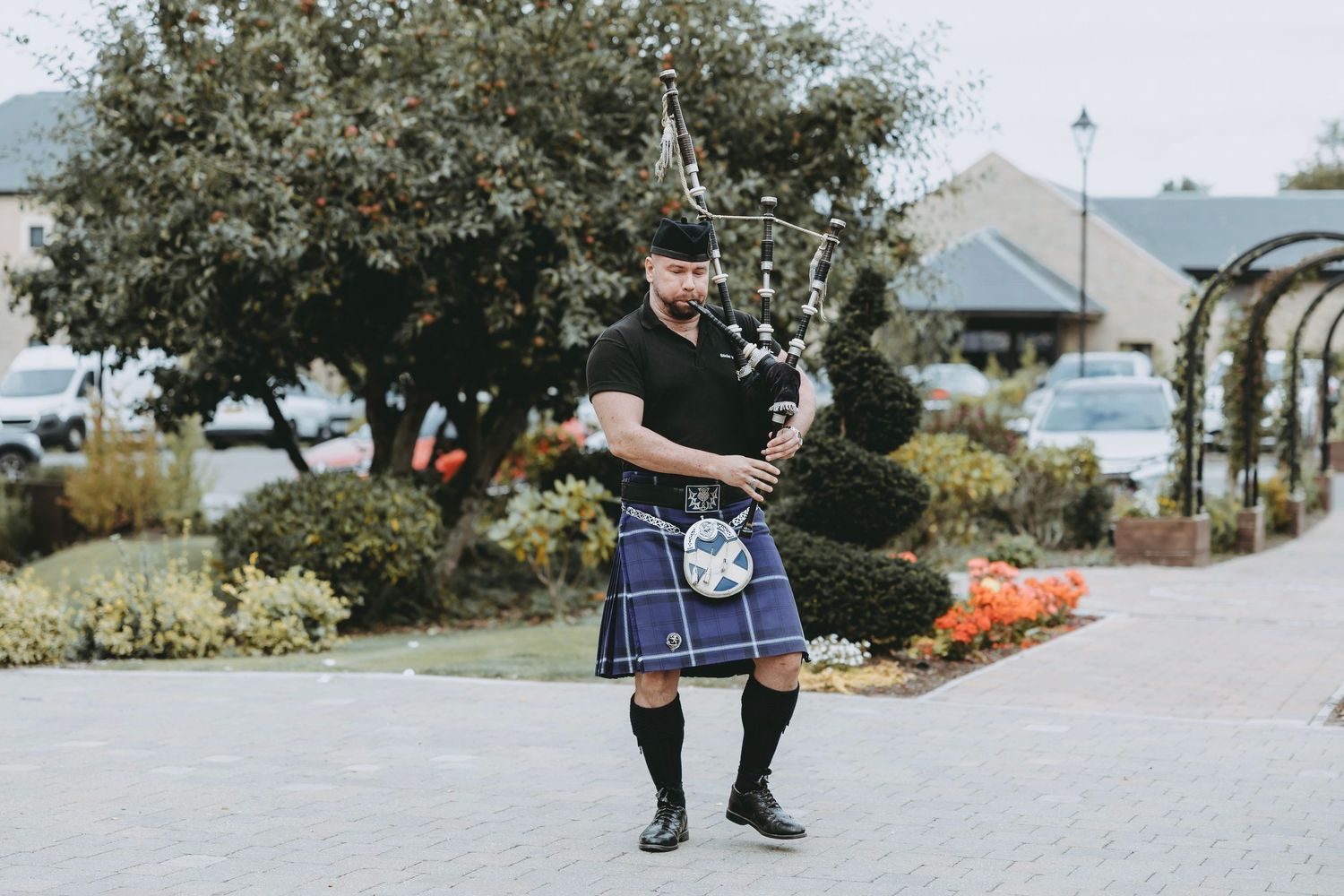Musicians in traditional Scottish attire walking along stone pathway.