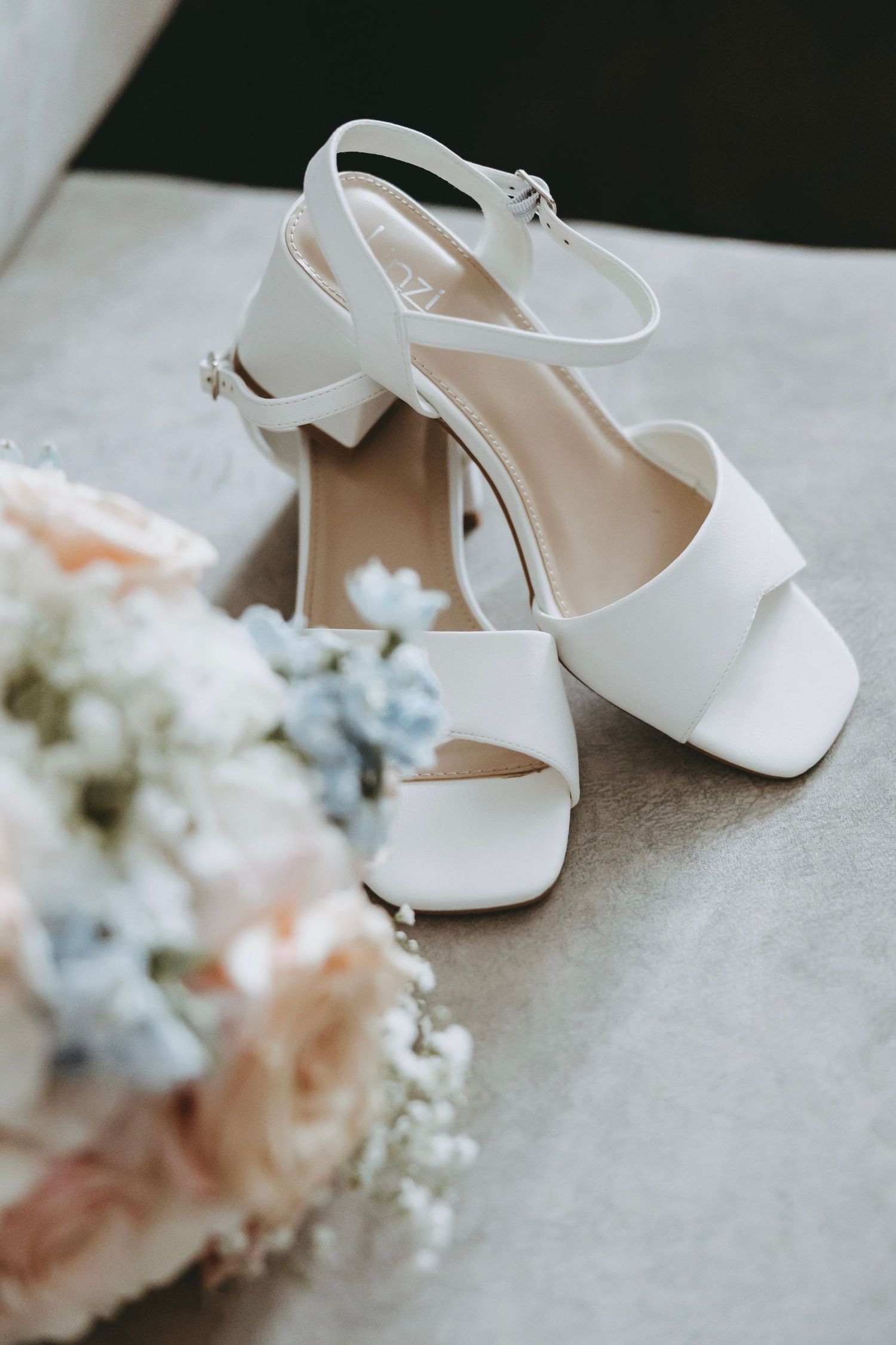 White bridal heels displayed next to delicate pink and white floral arrangements.