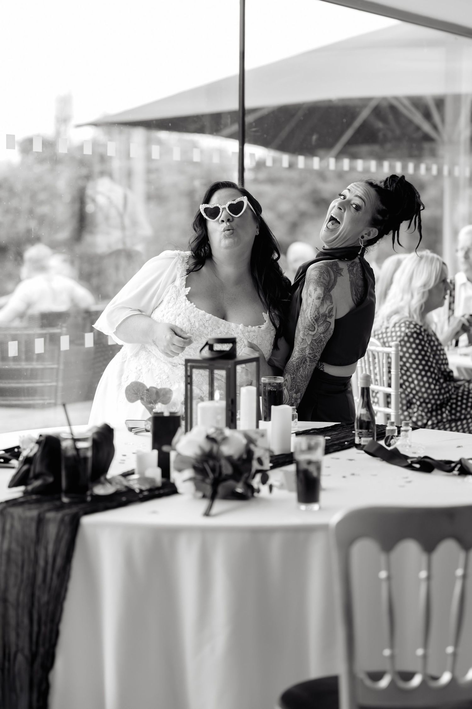 Black and white photo of guests posing playfully at a wedding reception table.