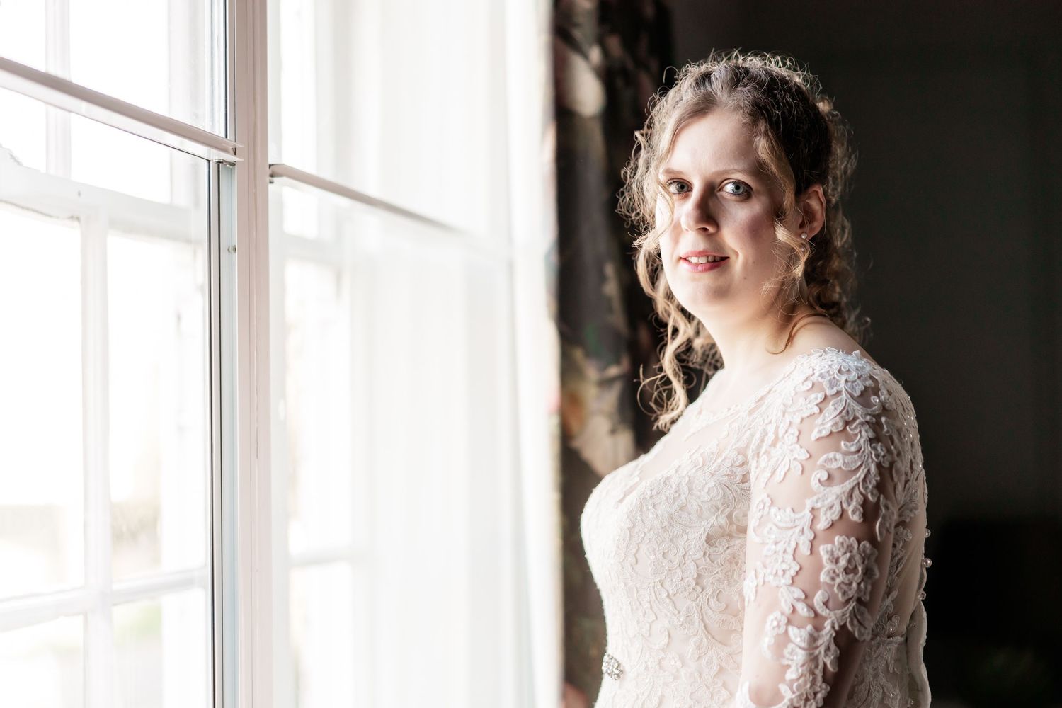 A lace wedding dress is captured in dramatic window lighting.