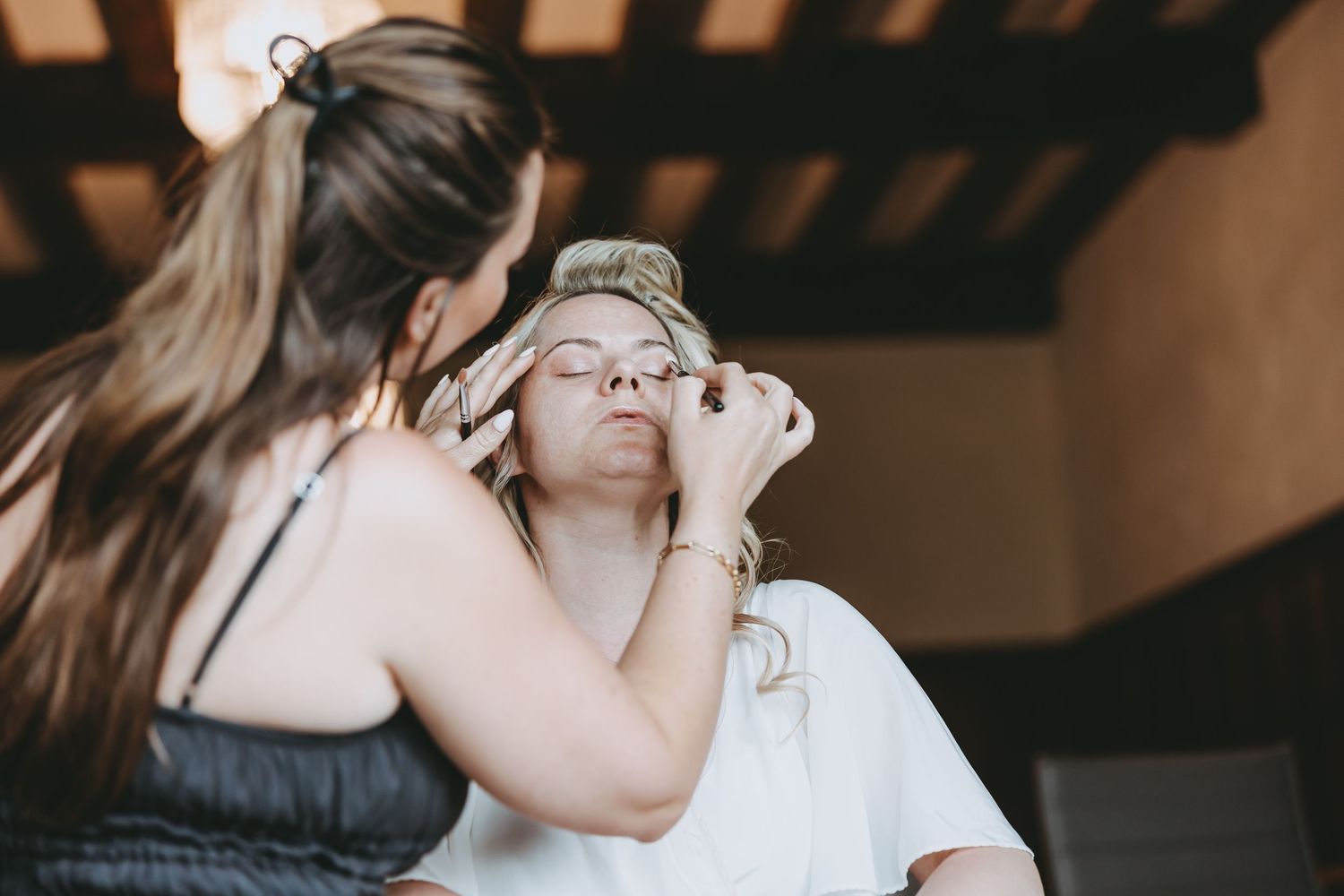 Makeup artist applies cosmetics to someone in a white dress during preparation.