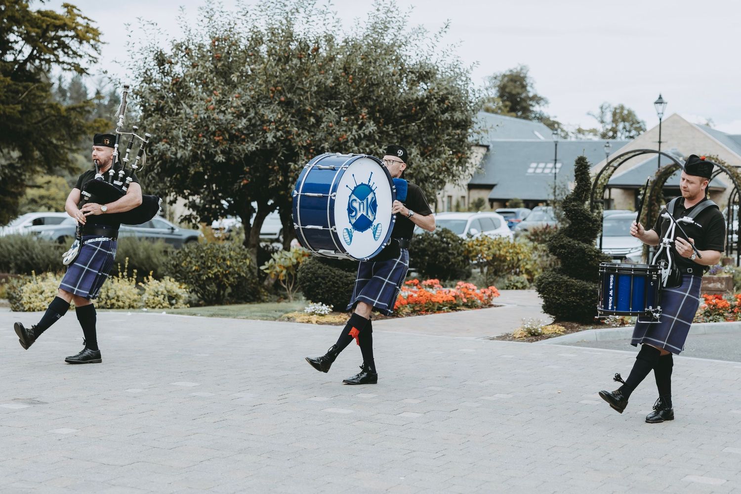 Three Scottish drummers in kilts marching with blue and white drums during a performance.