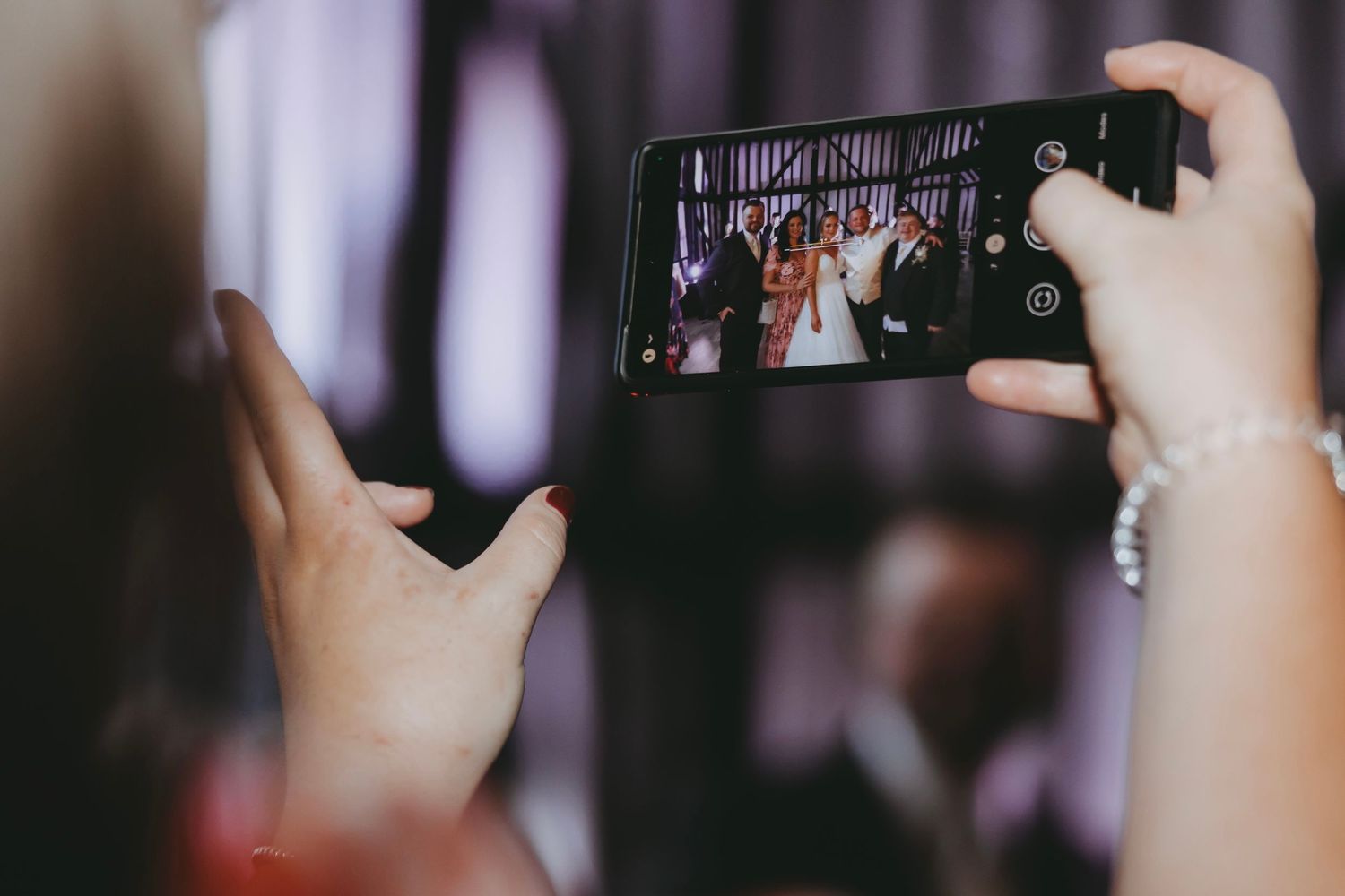 Guest capturing wedding moments on smartphone during celebration.