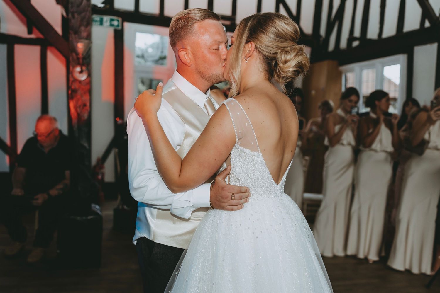 Wedding couple dancing in an elegant venue with exposed wooden beams and purple ambient lighting.