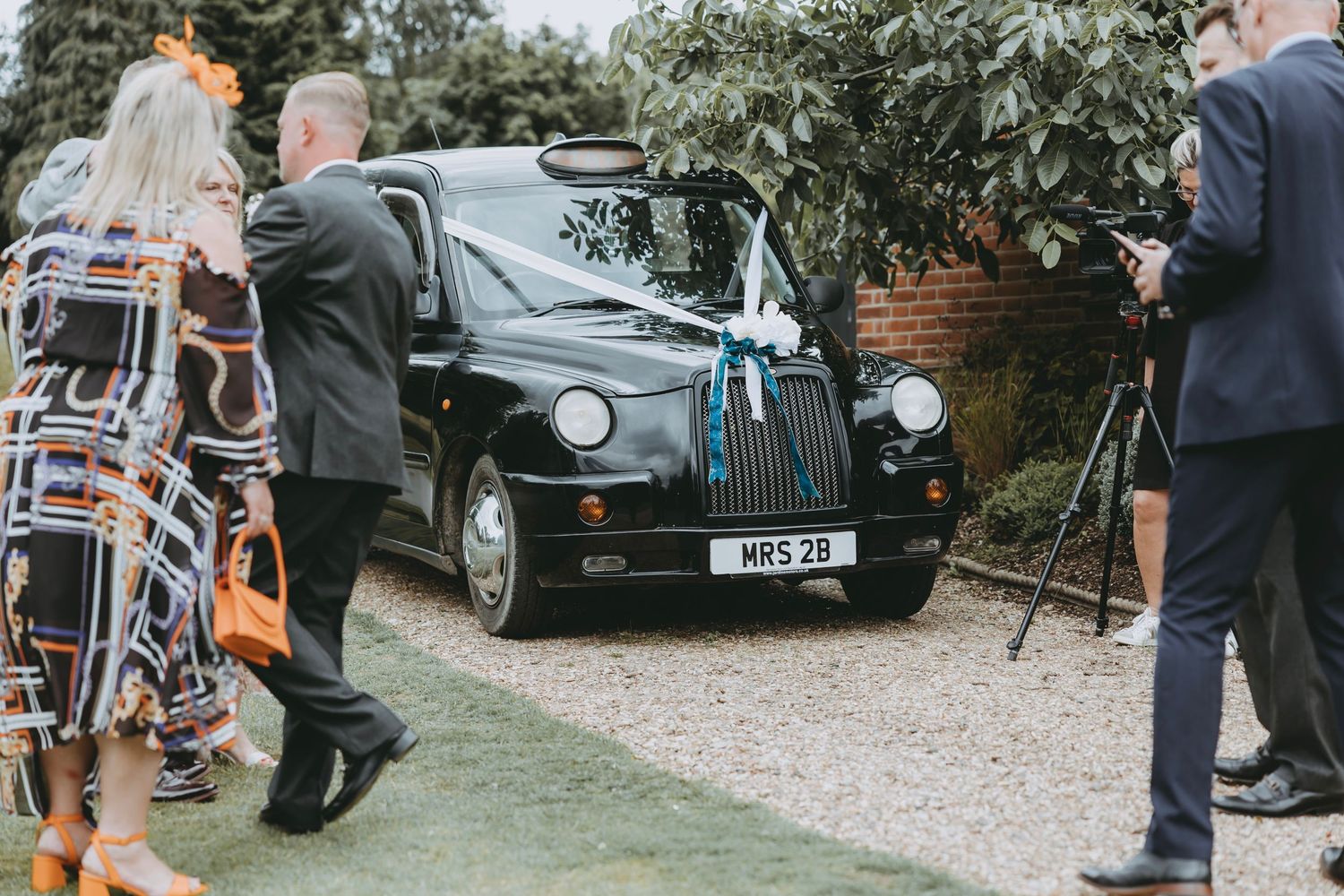 Vintage cars parked on gravel at an outdoor wedding venue with guests mingling in the background.