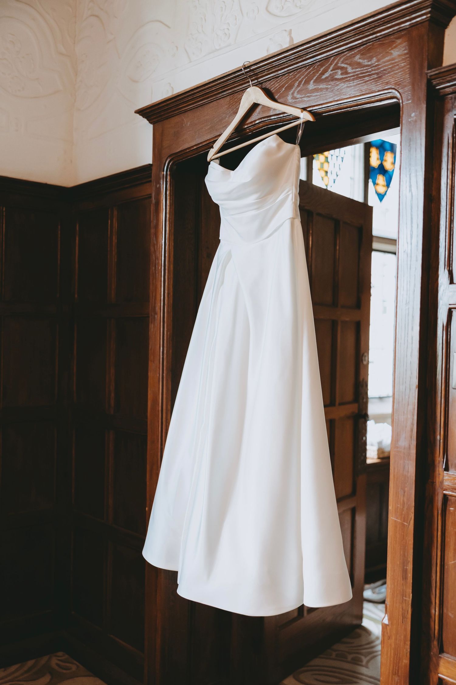 Multiple views of a white bridal gown displayed against rich wooden wall paneling.