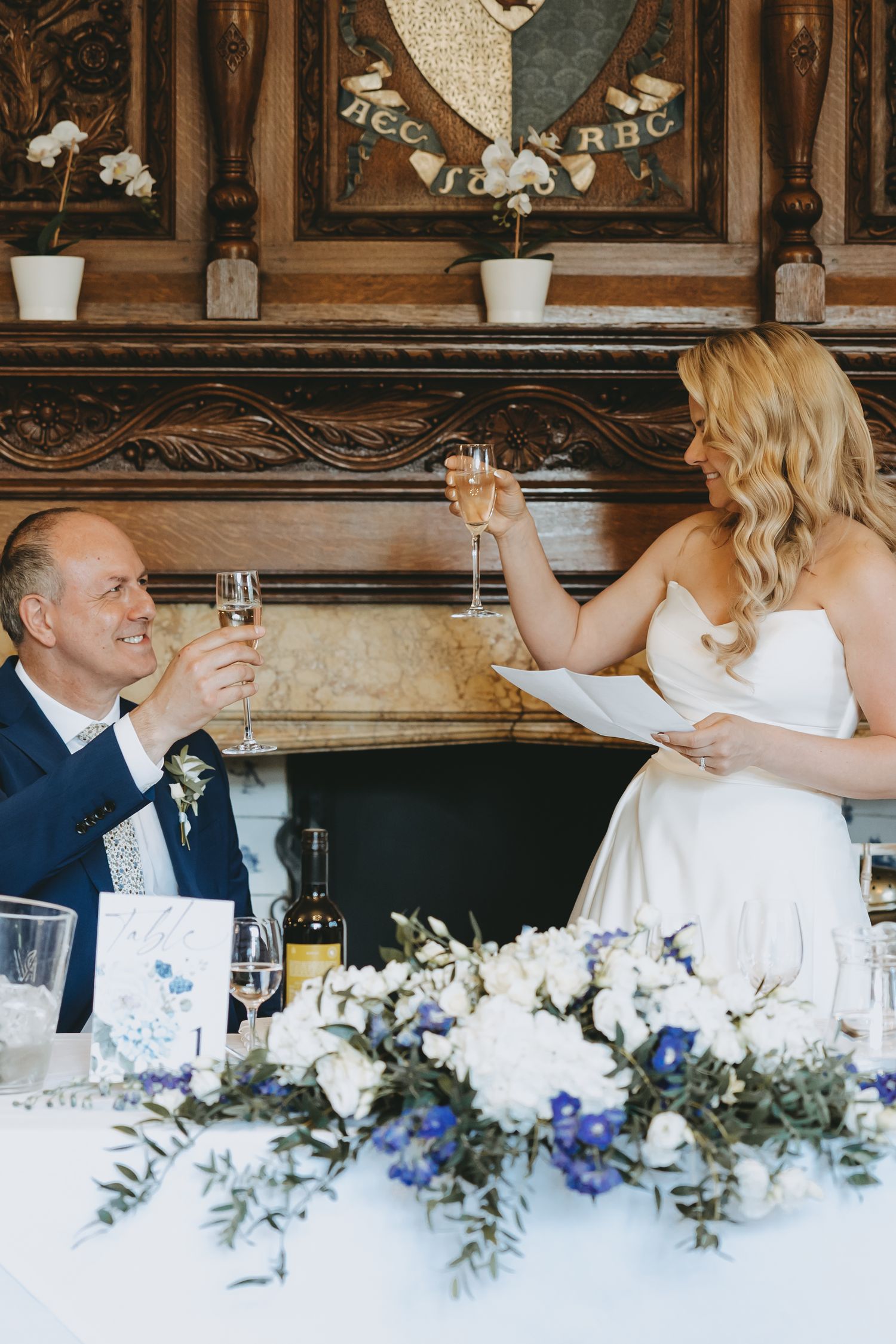 Wedding reception scene with floral centerpieces and guests toasting at an elegant venue at Fanhams Hall, Ware, Hertfordshire.