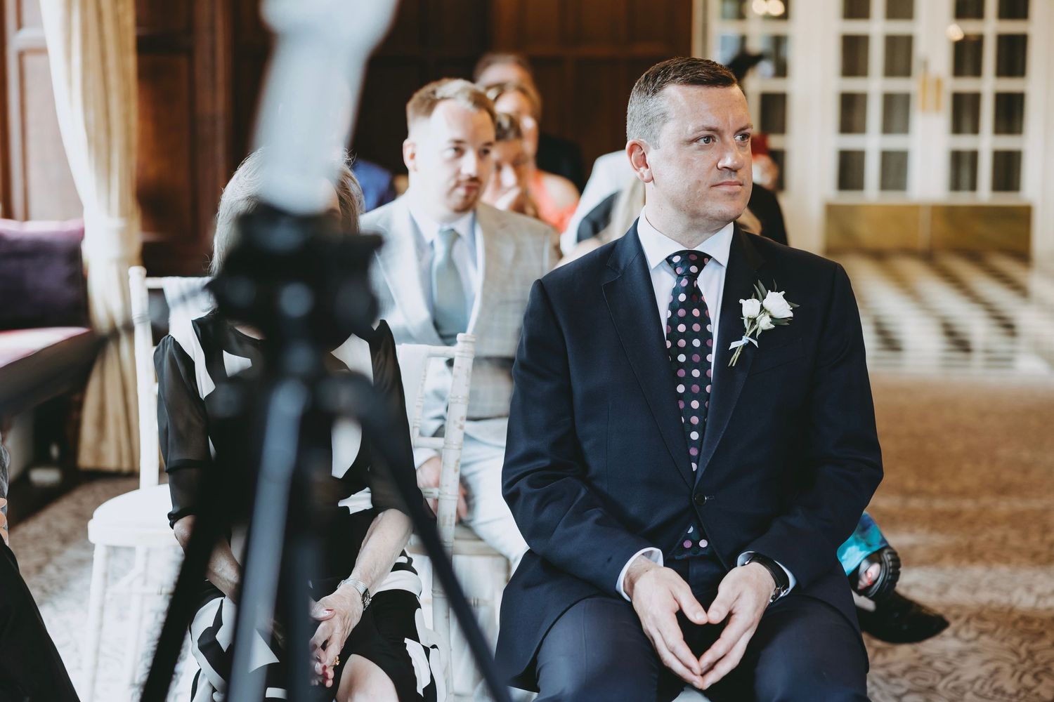 Wedding party gathered in an elegant wood-paneled room with chandelier overhead.