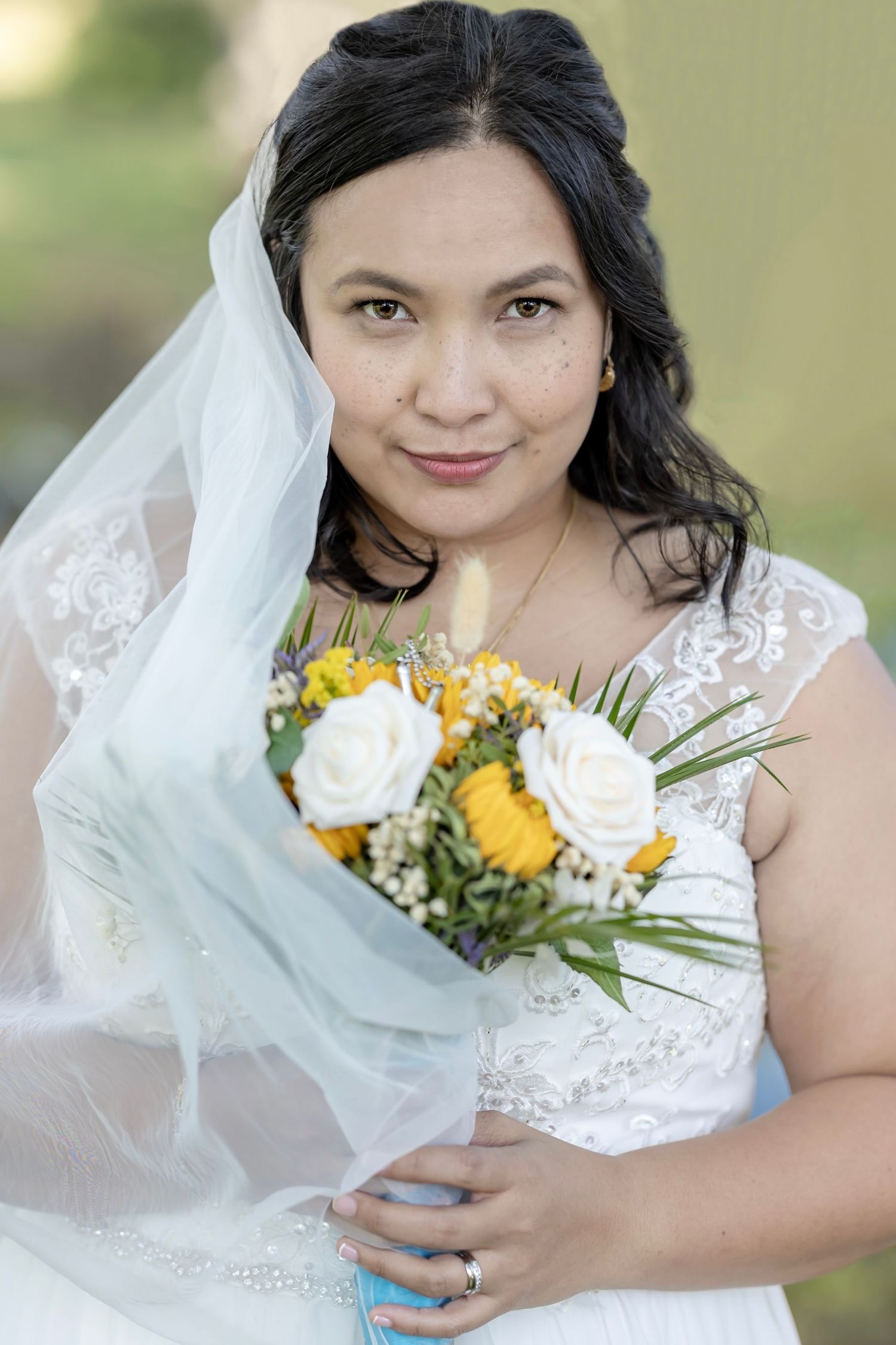 A bride poses with her yellow and white floral bouquet against a soft green background.