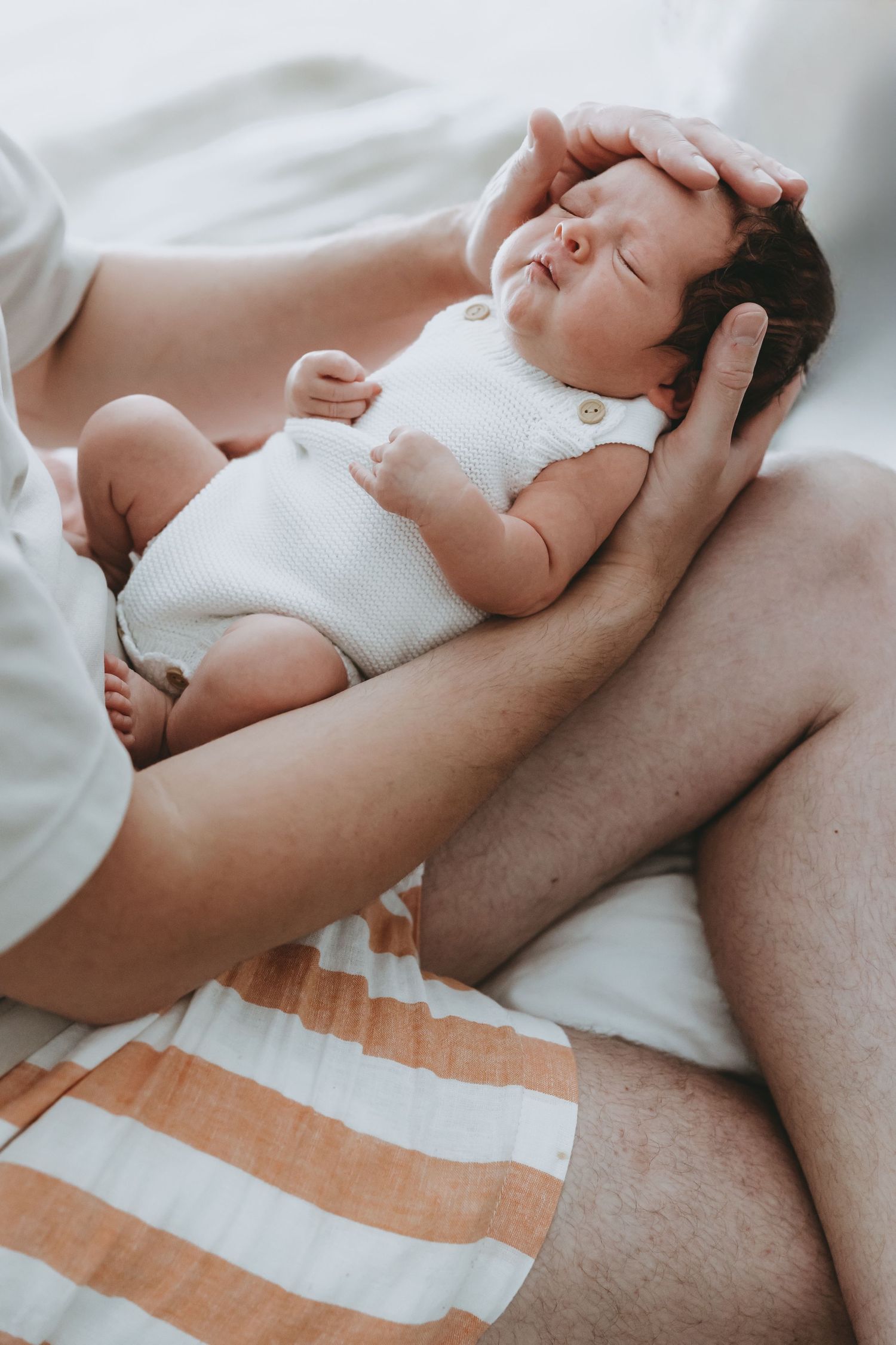 A series of intimate black and white photographs showing a newborn baby resting on soft white bedding.