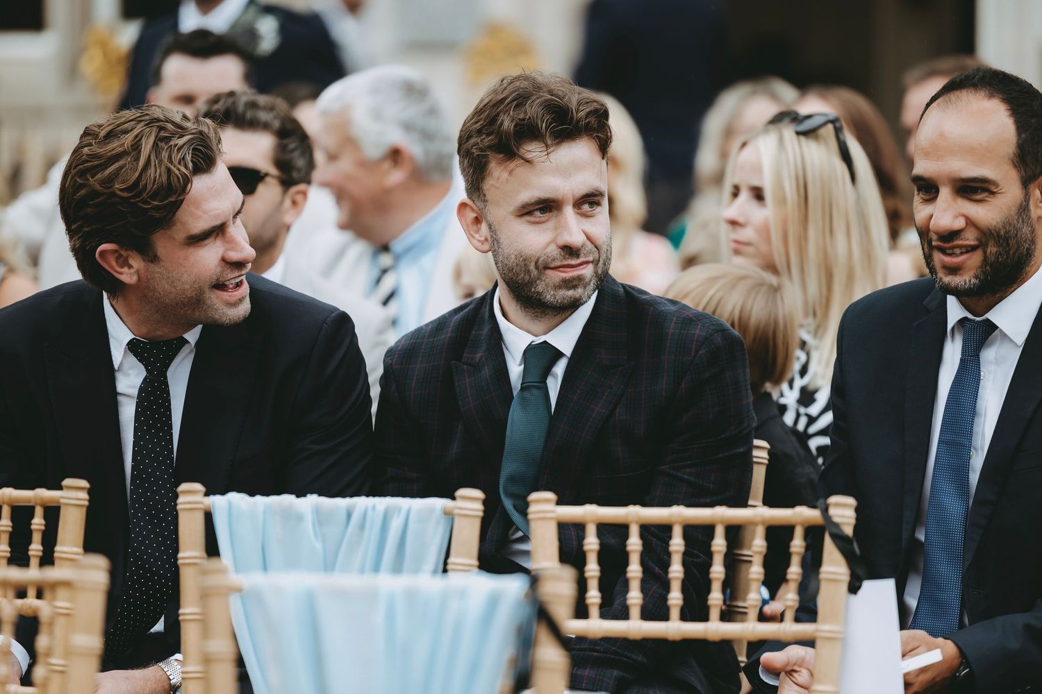 Wedding guests seated in rows of wooden chairs during an outdoor ceremony.