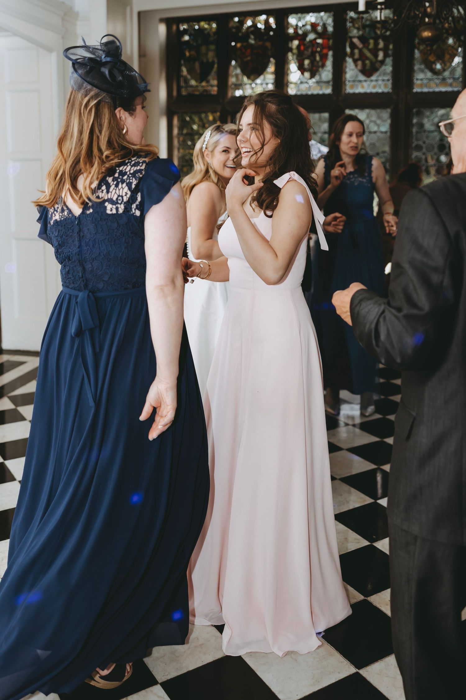 Wedding guests in navy blue dresses and formal wear gather on a checkered dance floor.