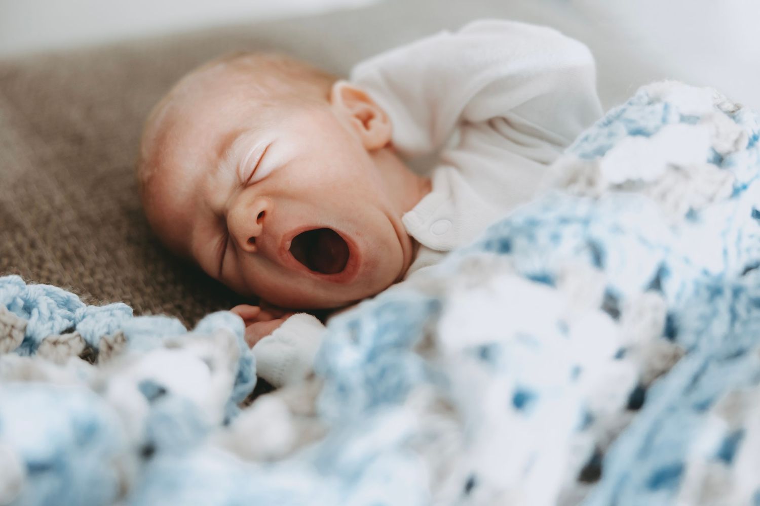 A sleeping baby yawns while laying on white bedding with blue floral patterns.