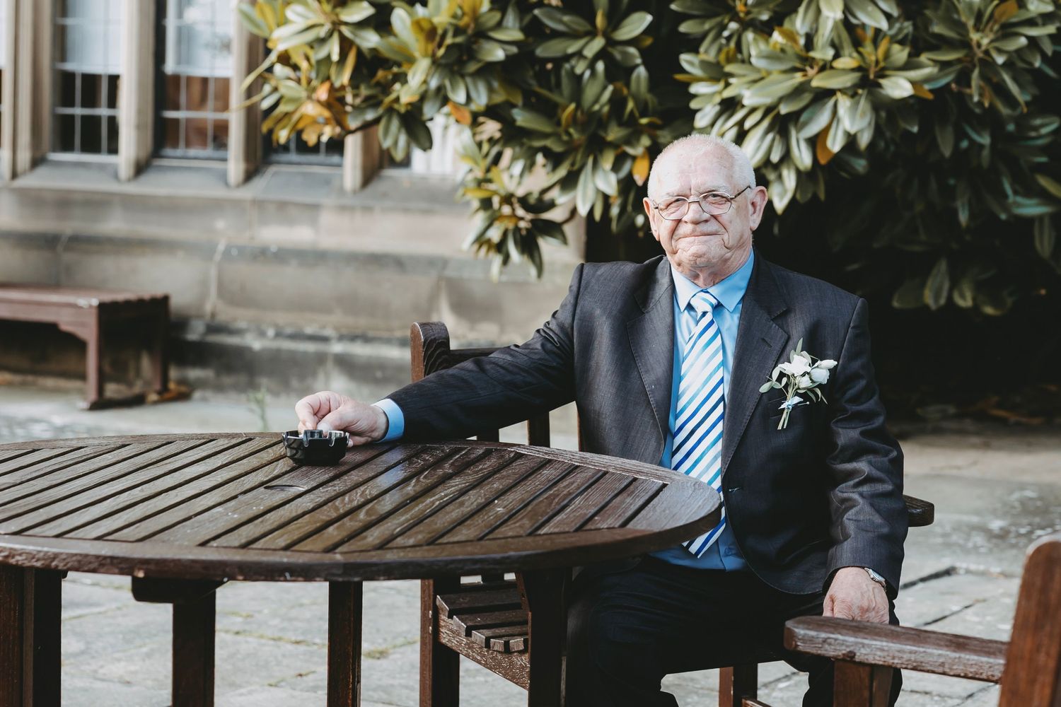 Person sitting alone on wooden benches near magnolia trees outside a building.