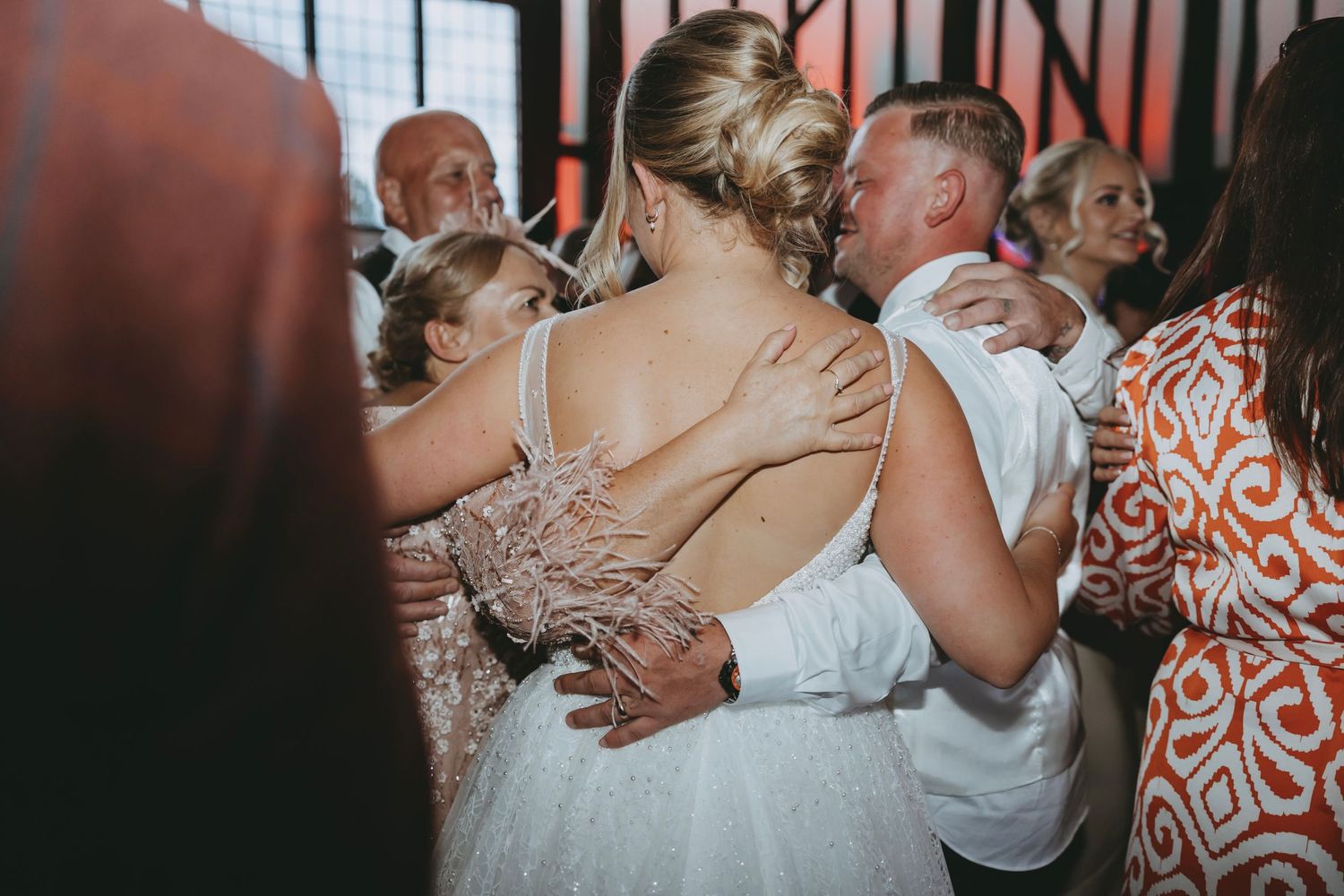 Couple embracing while dancing with wedding guests on crowded dance floor.