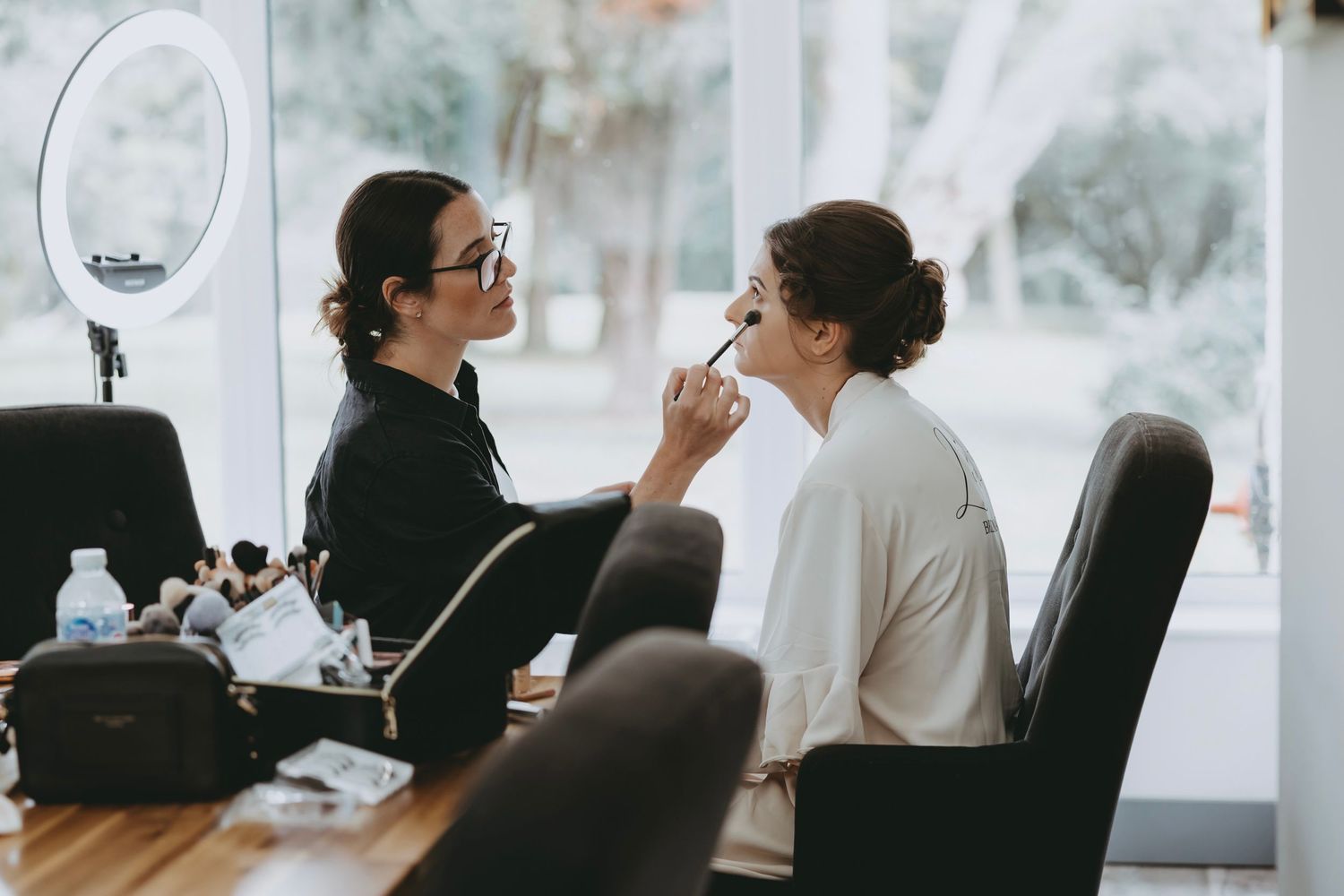 Professional makeup application session in progress with client seated in black chair.