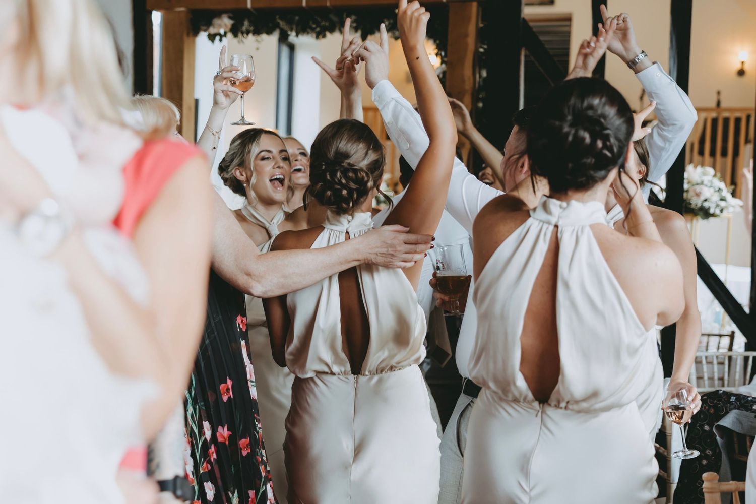 Wedding party guests dancing and celebrating in a modern venue with large windows.