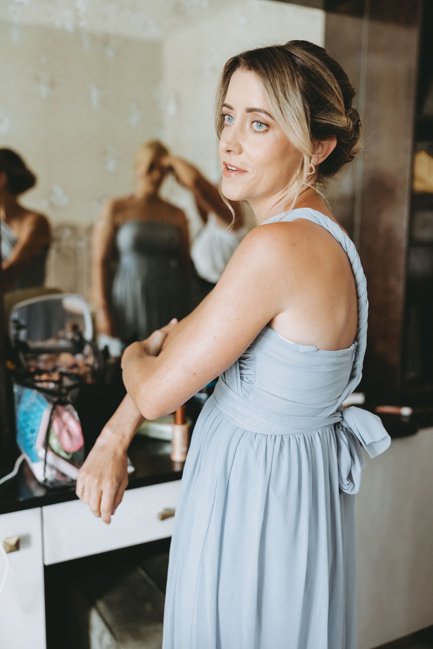 Someone in a light blue bridesmaid dress smiling while getting ready.