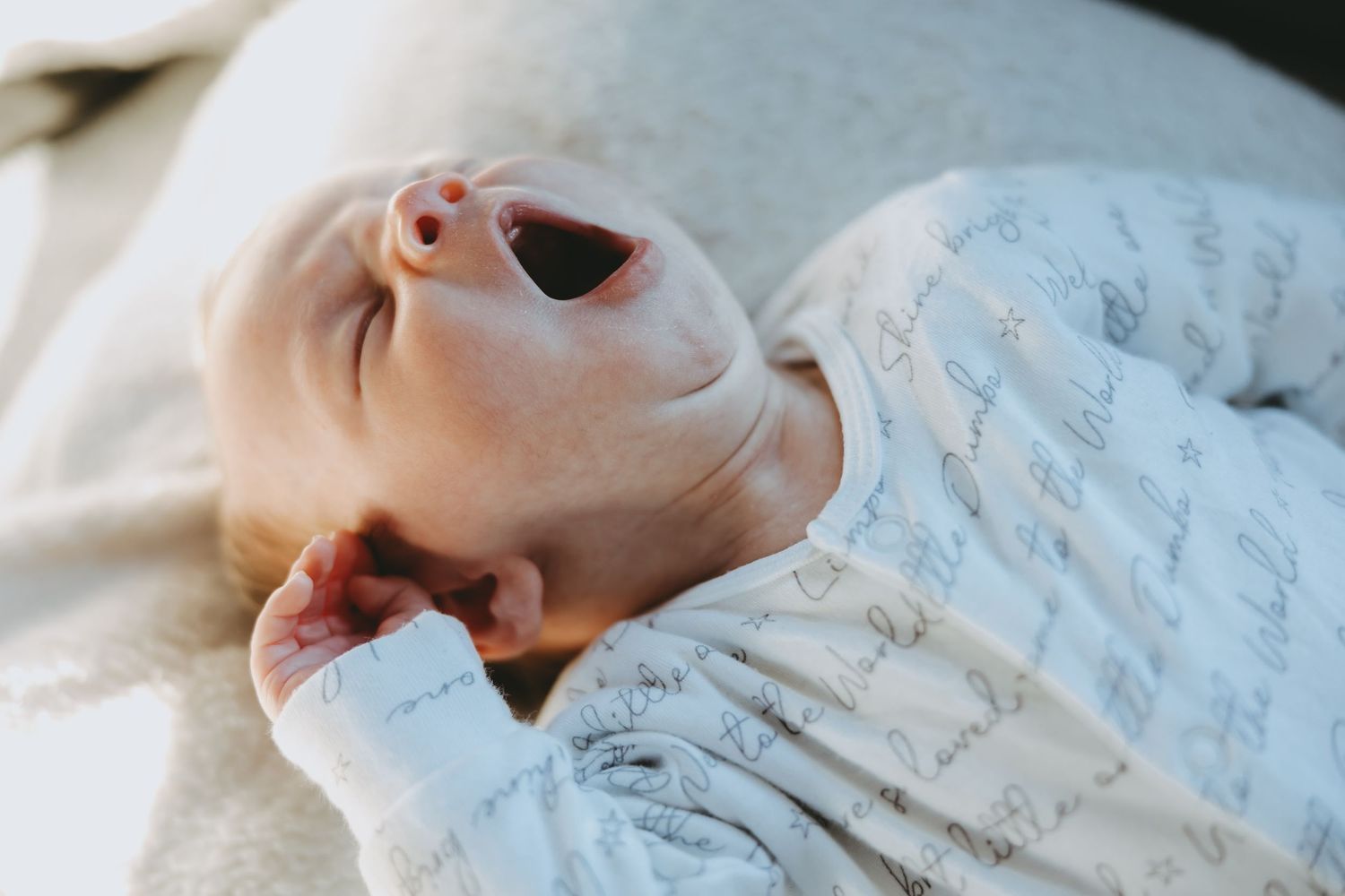 A baby sleeping peacefully in a white swaddle blanket with a soft, serene expression.