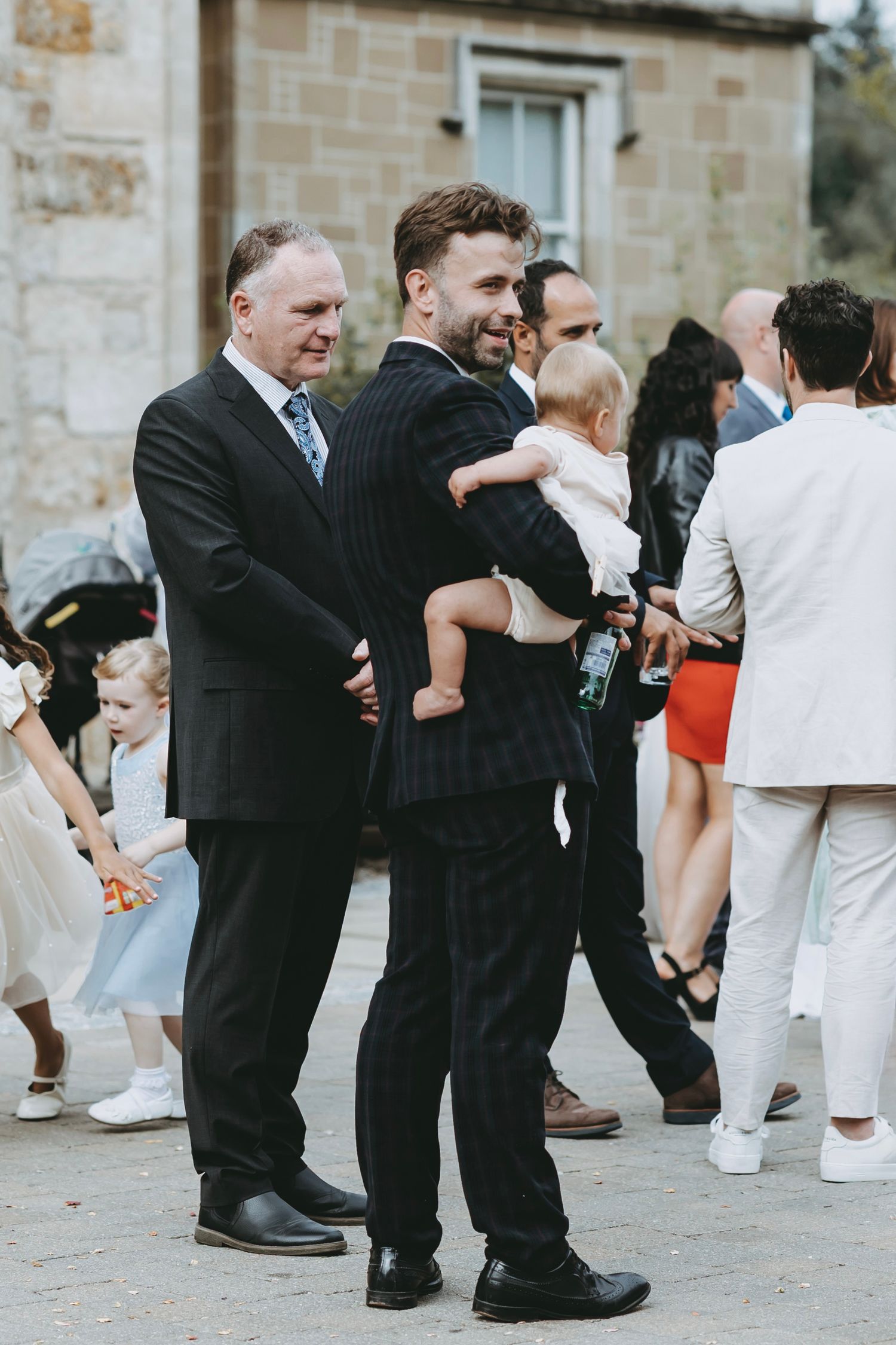 Wedding guests in formal attire dance and celebrate together at an elegant stone venue.