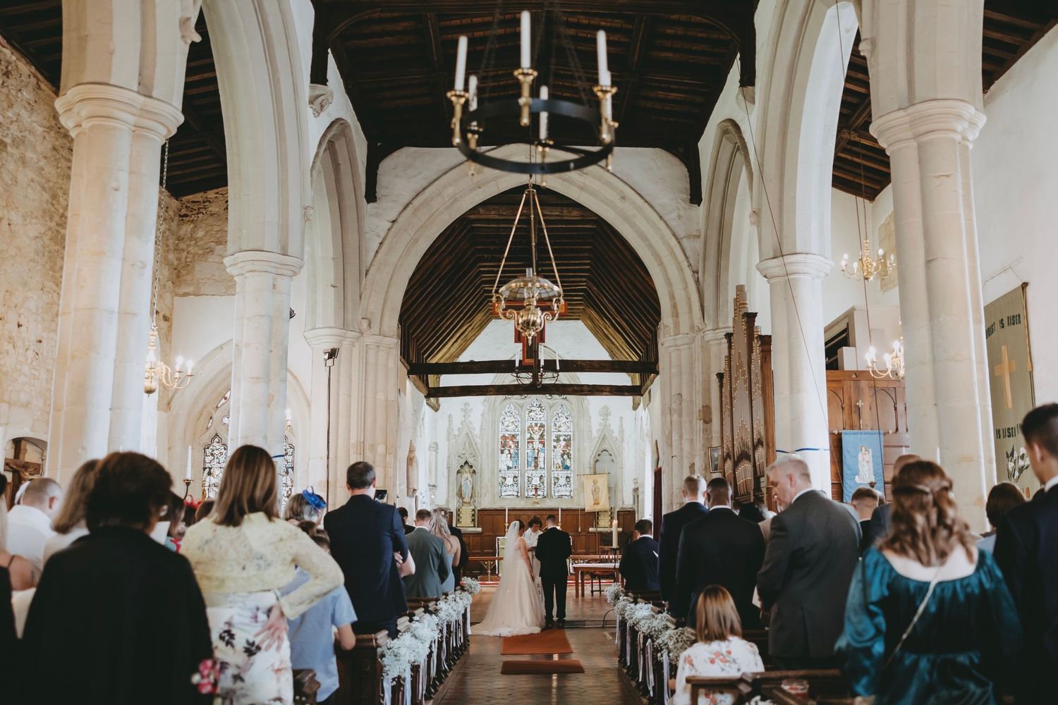 Wedding guests gather inside a historic church with white stone columns and vaulted ceilings.