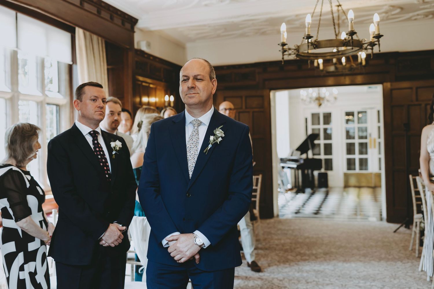 Wedding ceremony setup in an elegant room with wood paneling and chandeliers.