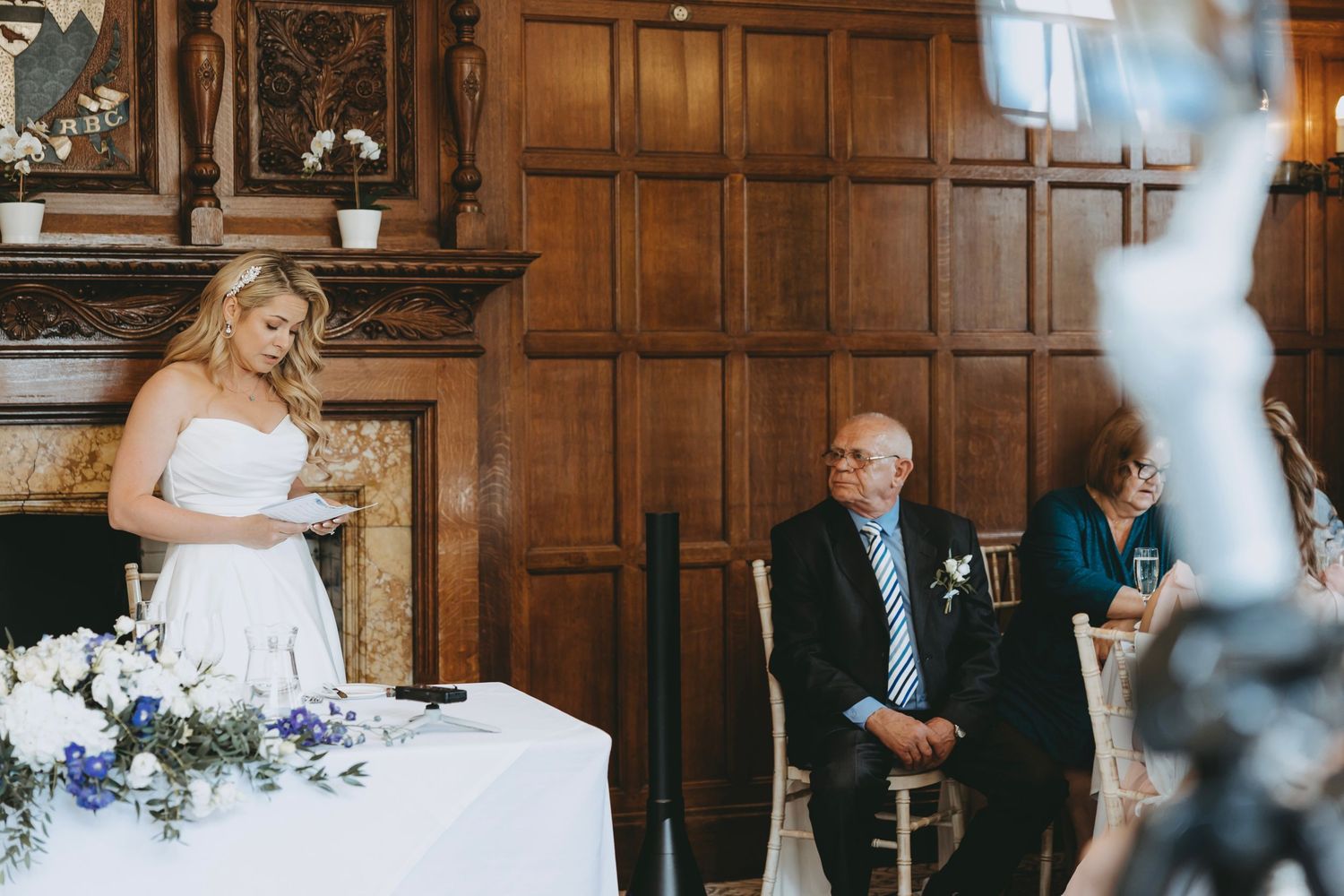 Elegant wedding reception setup with white linens and floral decor against wooden walls.