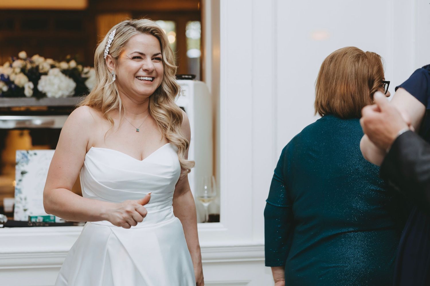 Wedding reception guests mingle in an elegant white-walled venue with formal decor.